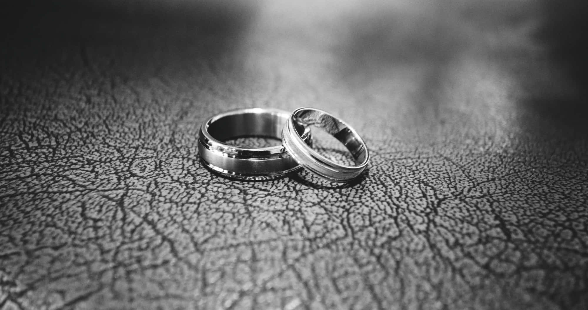 結婚戒指 桌布 壁紙 — 兩枚結婚戒指在柔和光線下放置於龜裂皮革上，以單色特寫呈現。