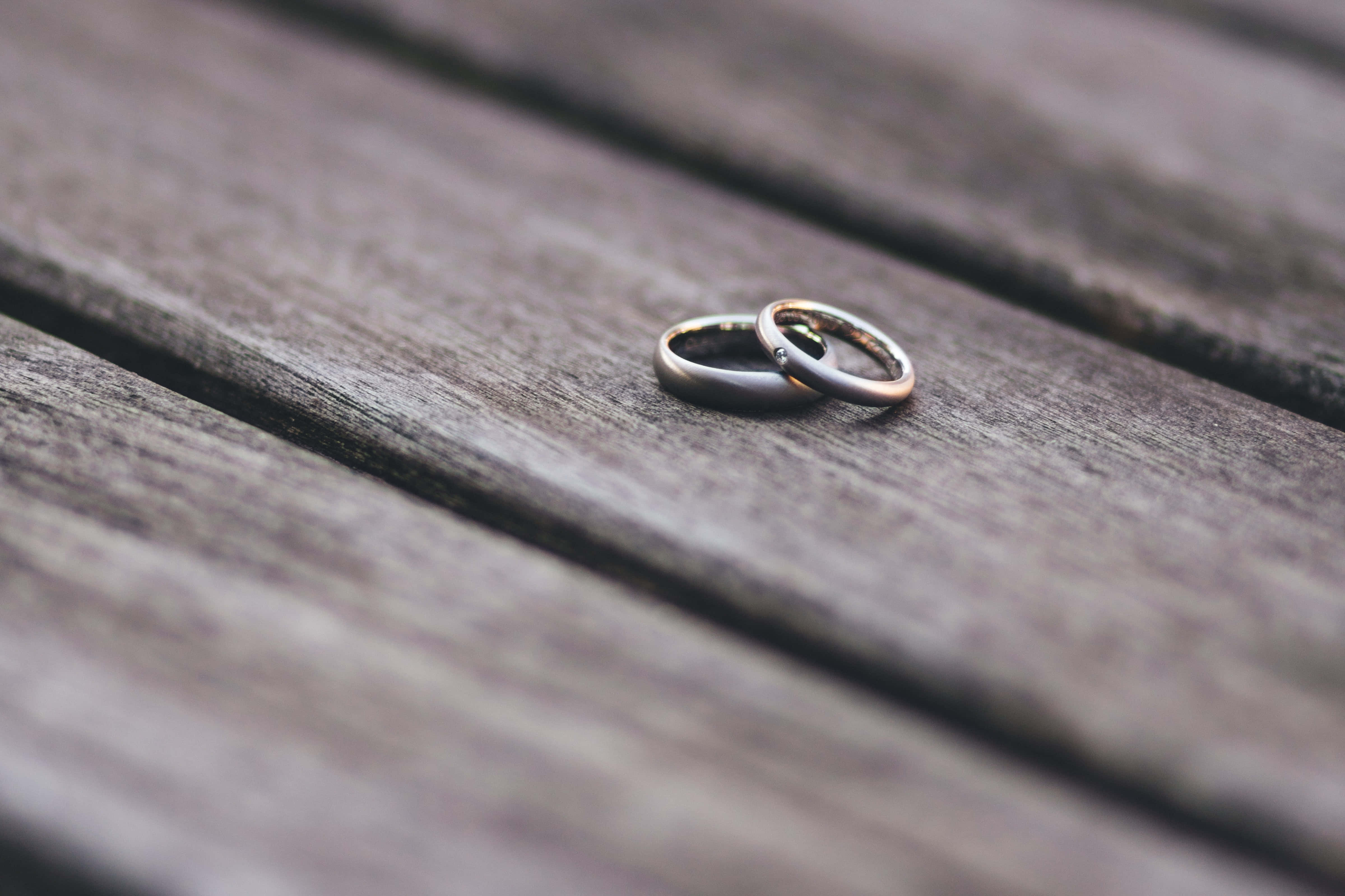 Wedding Rings 桌布 壁紙 — 兩枚結婚戒指在柔和的自然光下交織在一起，放在風化的木質表面上。