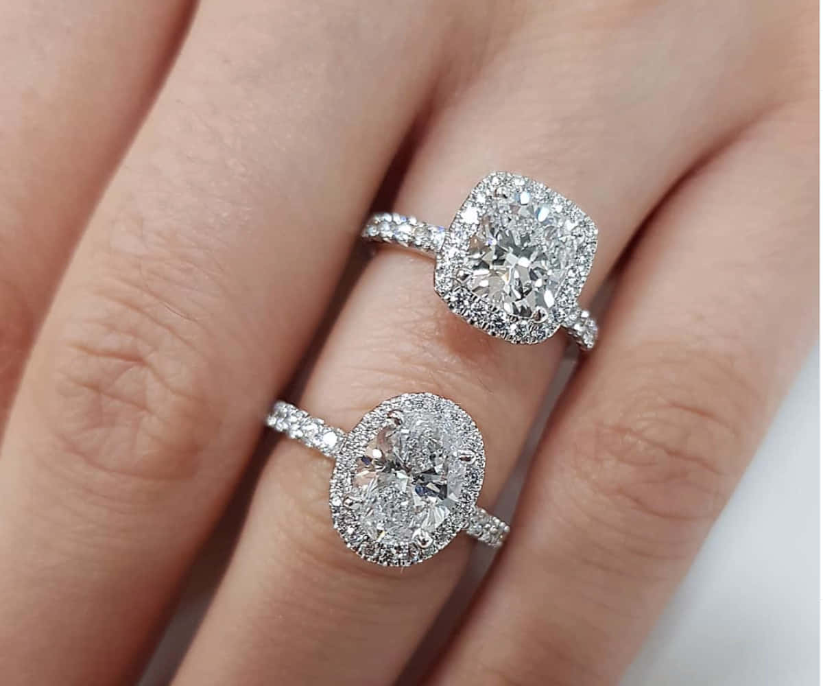 rings 桌布 壁紙 — 兩枚耀眼奪目的鑽石訂婚戒指，採用光環鑲嵌，優雅地放在女士手上，在柔和光線下閃閃發光。