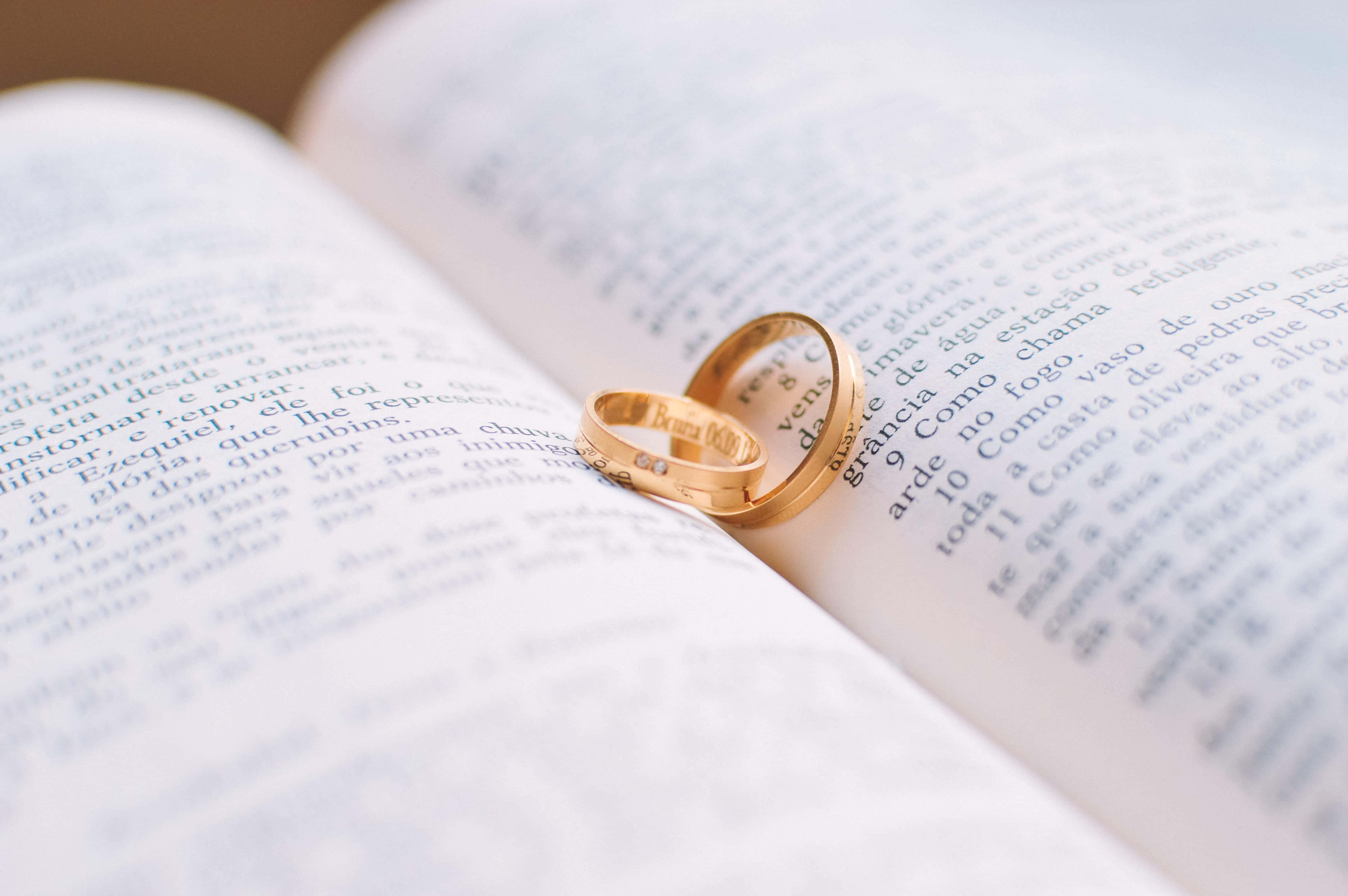 Ring 桌布 壁紙 — 兩枚金婚戒親密地放在一本打開的書頁上，伴隨著柔和自然光。