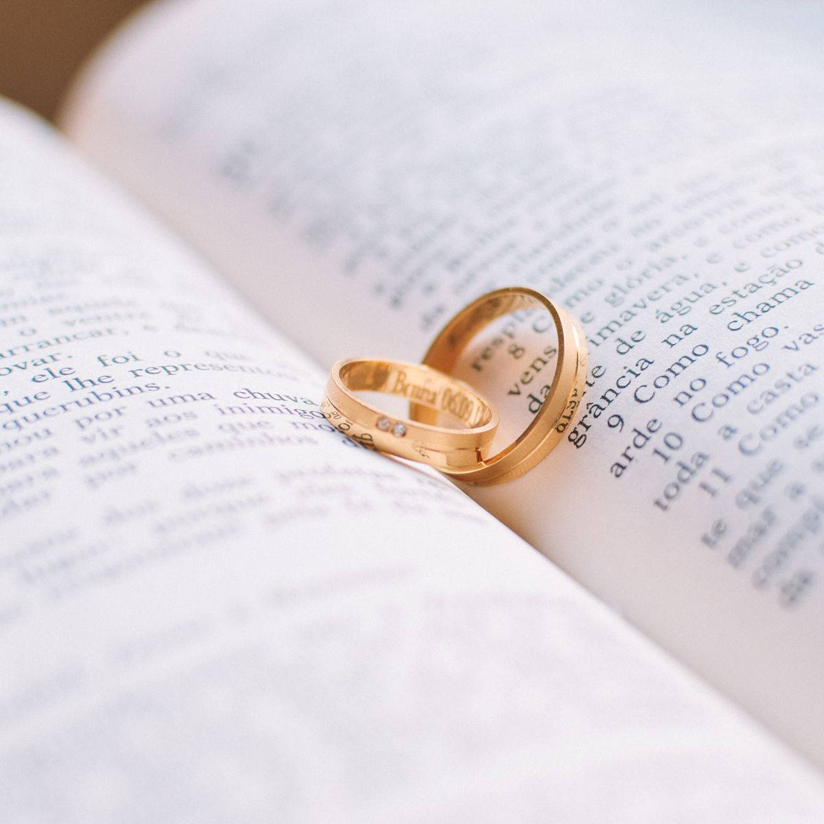 Wedding Rings 桌布 壁紙 — 兩枚金婚戒親密地放在一本有葡萄牙語文字的書的打開頁面上。