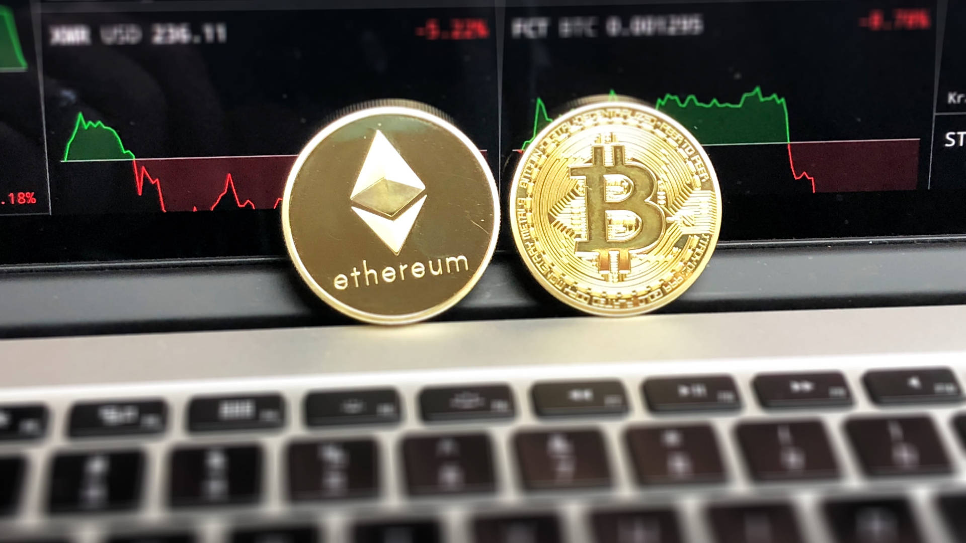 以太坊 桌布 壁紙 — 兩枚金色加密貨幣以太坊和比特幣放在筆記型電腦鍵盤上，背後有股市圖表發光。