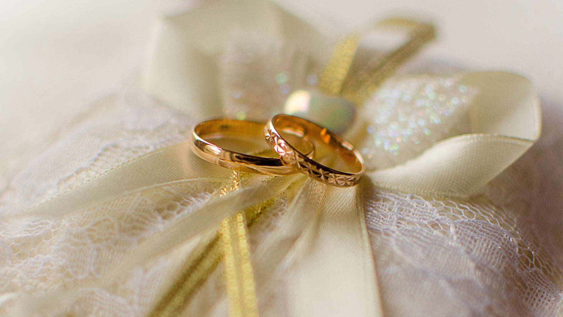 高清 桌布 壁紙 — 兩枚金色結婚戒指優雅地放在飾有閃亮元素的奶油色蕾絲和絲帶上。
