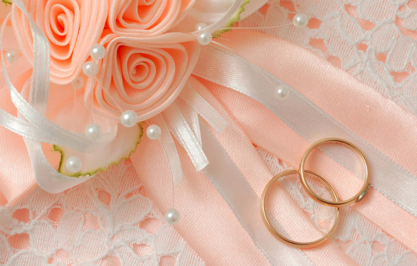 Marriage 桌布 壁紙 — 兩枚金色結婚戒指放在蜜桃色緞面玫瑰和珍珠裝飾旁，置於精緻蕾絲上。