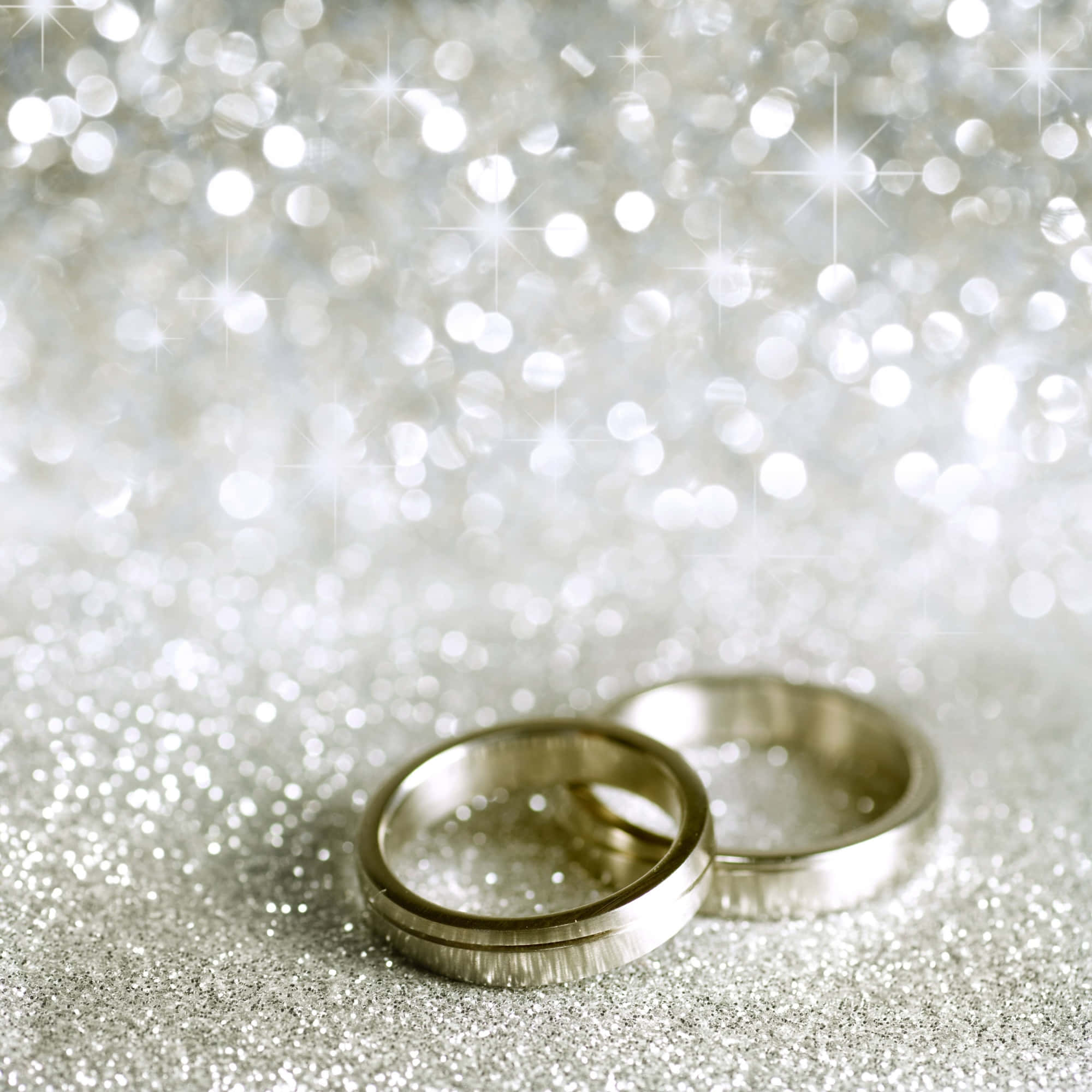 結婚戒指 桌布 壁紙 — 兩枚銀色結婚戒指放在閃閃發光的銀色表面上，背景有閃爍的散景燈光。