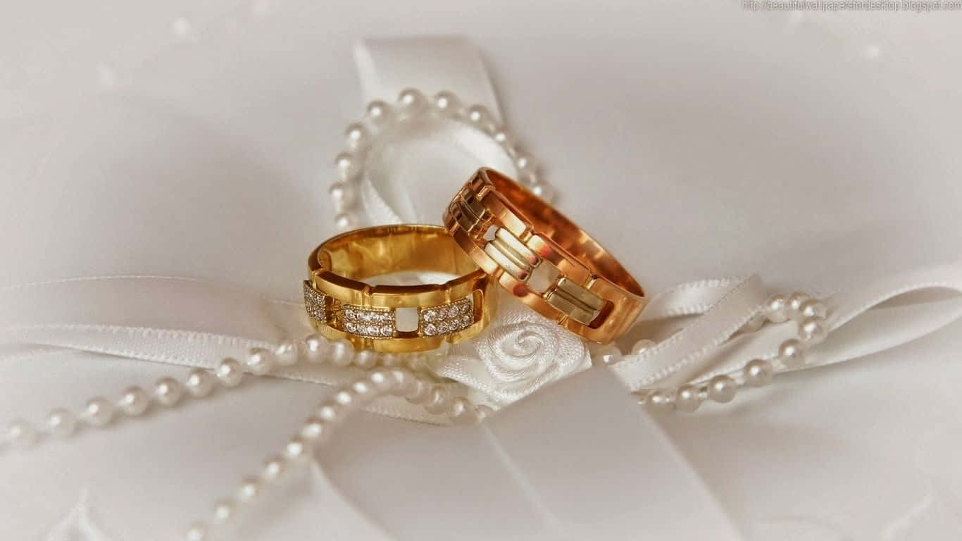 Marriage 桌布 壁紙 — 兩枚鑲有鑽石的金色結婚戒指優雅地放置在白色緞帶和珍珠鏈上。