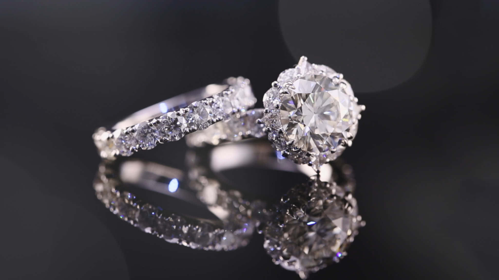 Ring 桌布 壁紙 — 兩枚閃爍的鑽石戒指在帶有柔和散景背景的反射黑色表面上閃耀。
