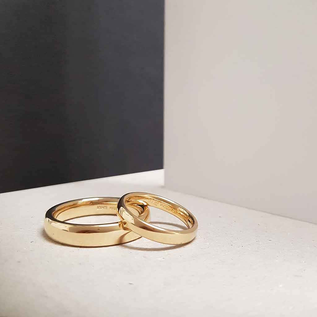 Wedding Rings 桌布 壁紙 — 兩枚閃閃發光的金色結婚戒指交織在極簡白色表面上，襯托出鮮明的黑白背景。