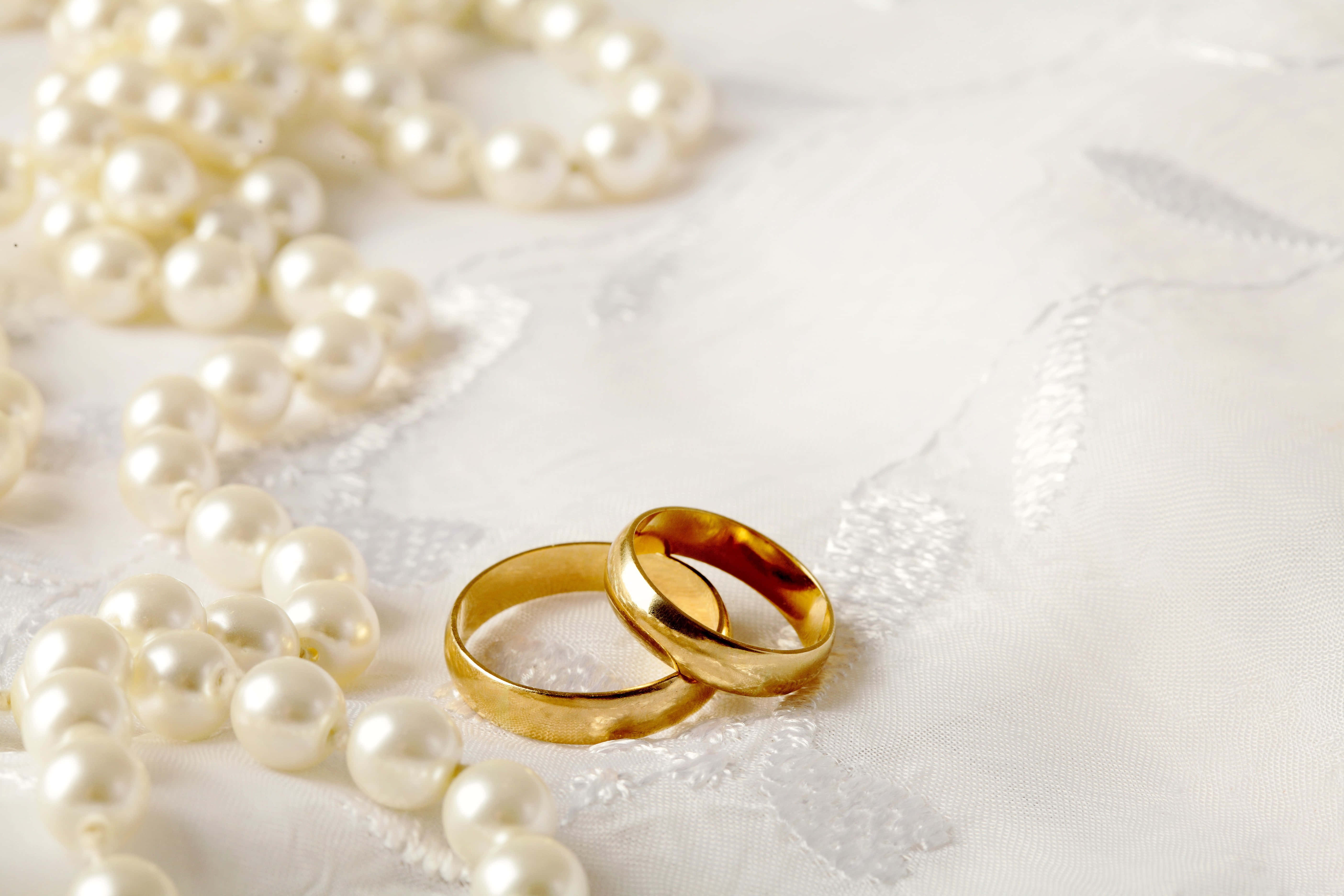 pearl 桌布 壁紙 — 兩枚閃閃發光的黃金結婚戒指放在精緻的白色蕾絲上，旁邊是一串光澤的珍珠。