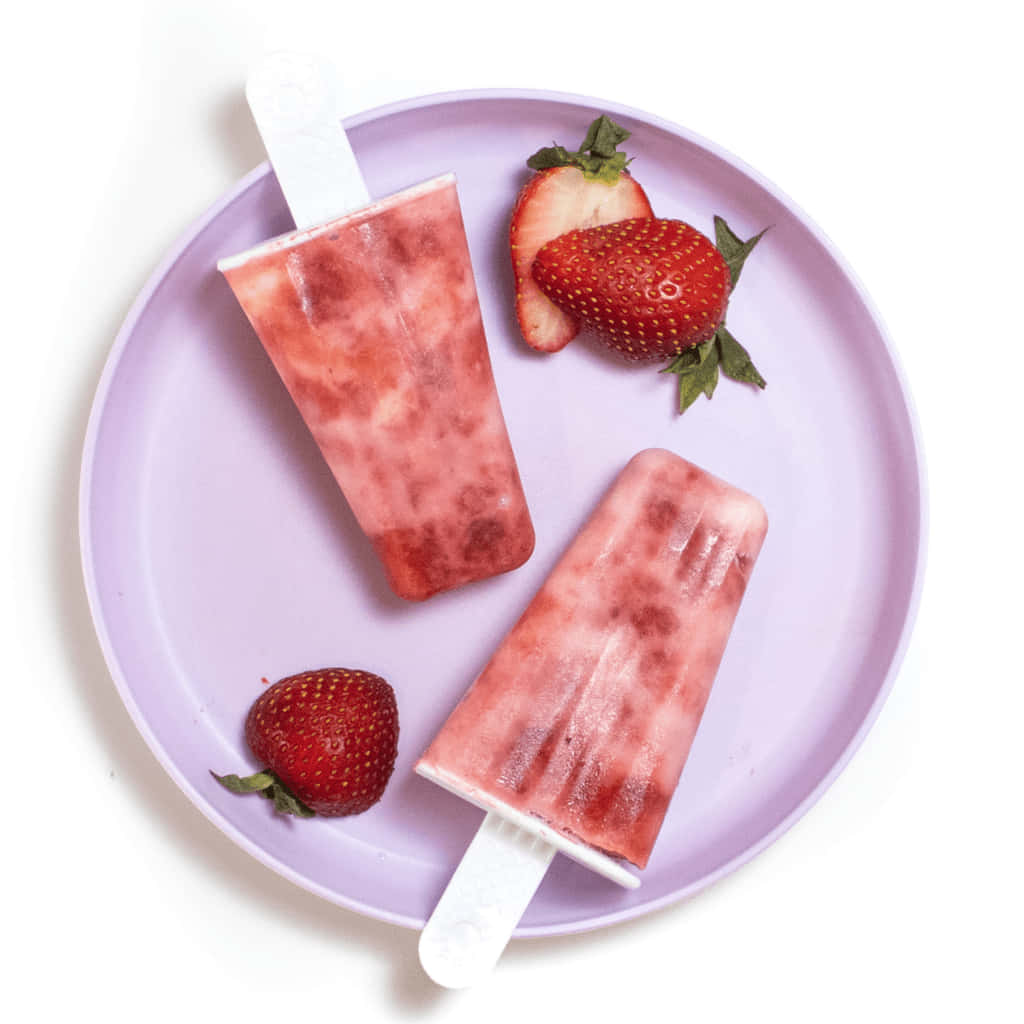 Strawberries 桌布 壁紙 — 兩枝草莓冰棒放在薰衣草色盤子上，旁邊有新鮮整顆和切片草莓，背景是純白色。