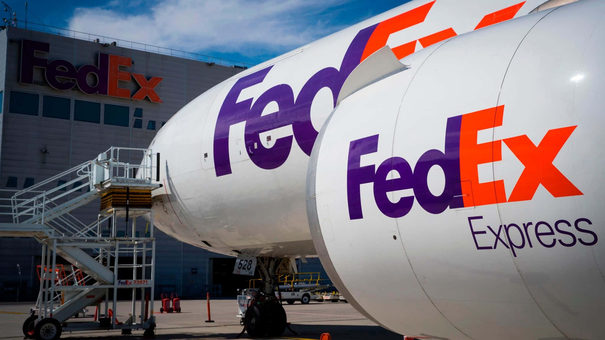 聯邦快遞 桌布 壁紙 — 兩架 FedEx Express 貨機停泊在機場閘口，背景是 FedEx 大樓，天空清澈湛藍。