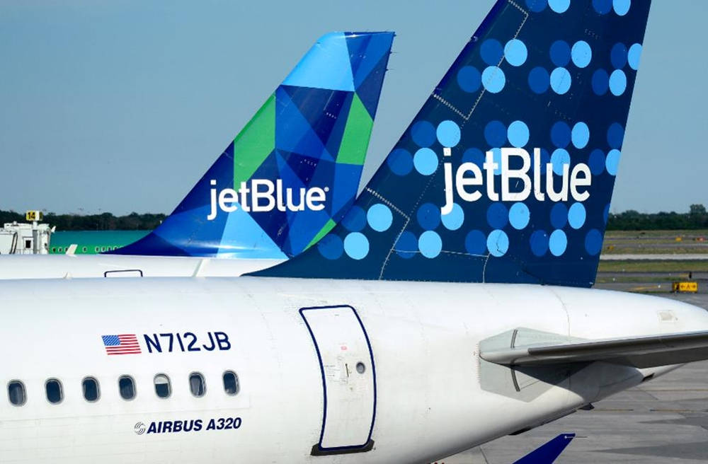 Polka Dot 桌布 壁紙 — 兩架 JetBlue 空中巴士 A320 飛機尾部帶有藍綠色幾何圖案和藍色圓點塗裝，停在停機坪上，天空晴朗。