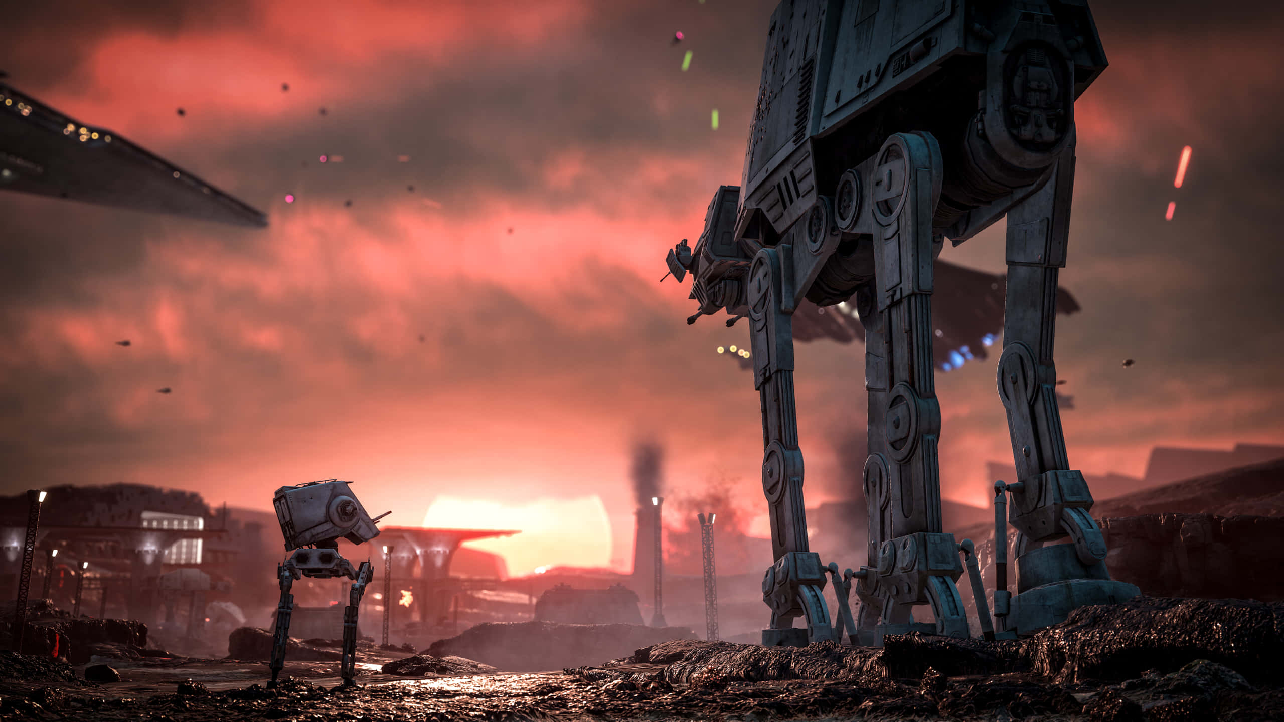 Star Wars Games 桌布 壁紙 — 兩架AT-AT步行機矗立在荒涼的戰場上，天空是火紅的日落，遠處有船隻和煙霧。