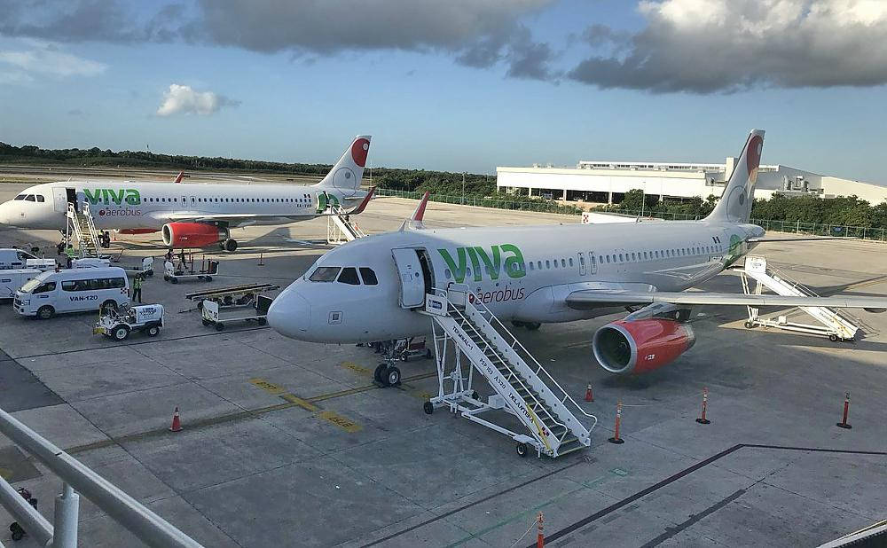 飛機 桌布 壁紙 — 兩架Viva Aerobus飛機停在機場閘口，配有移動樓梯和地勤車輛，天空局部多雲。