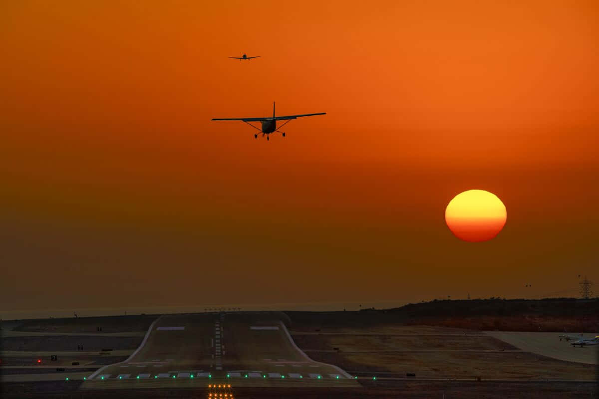 Airport 桌布 壁紙 — 兩架小型飛機在火紅的橙色日落中翱翔，太陽低垂在機場跑道上。
