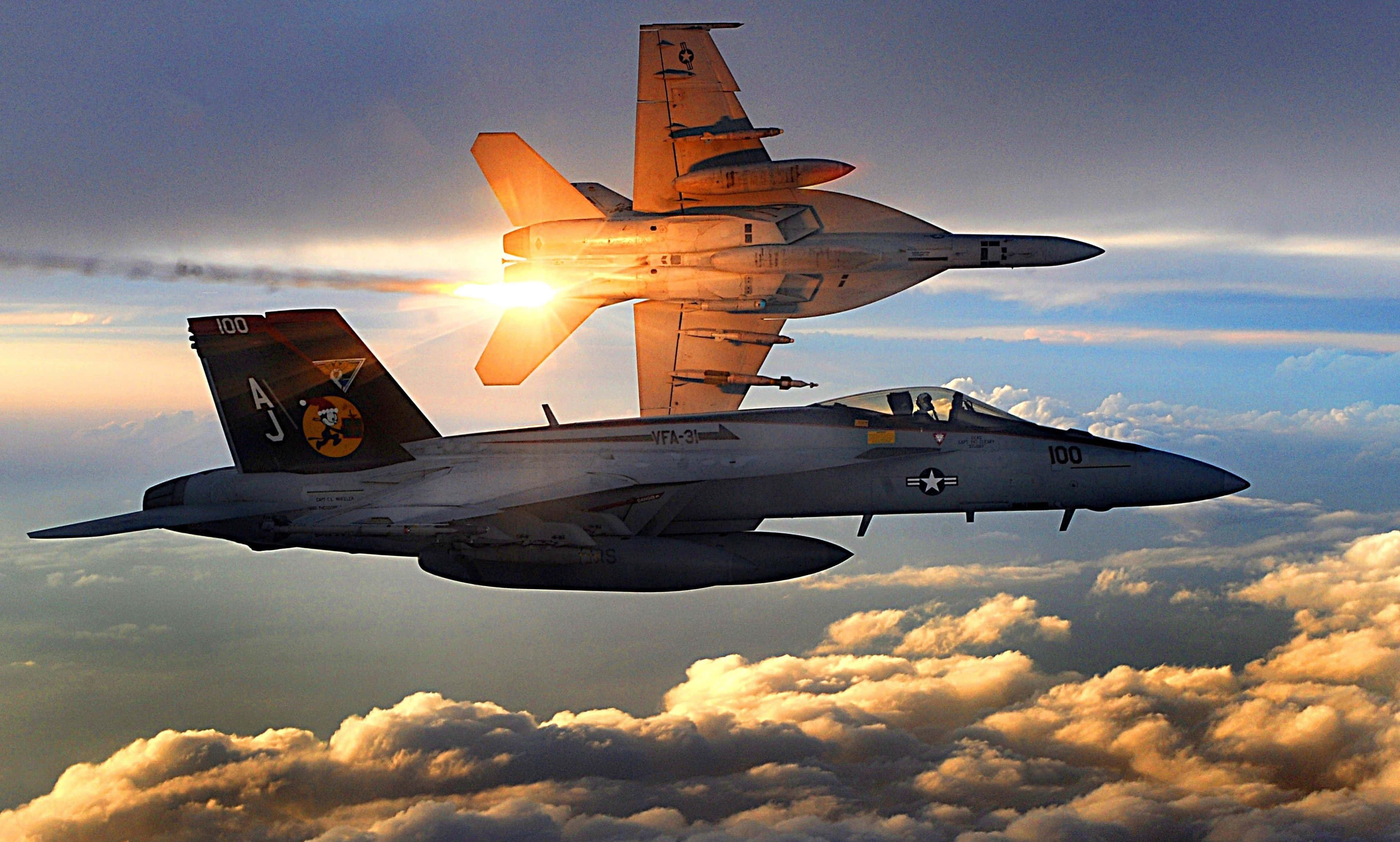 Military Plane 桌布 壁紙 — 兩架戰鬥機在日落雲層中翱翔，太陽在其中一架飛機後方發光。