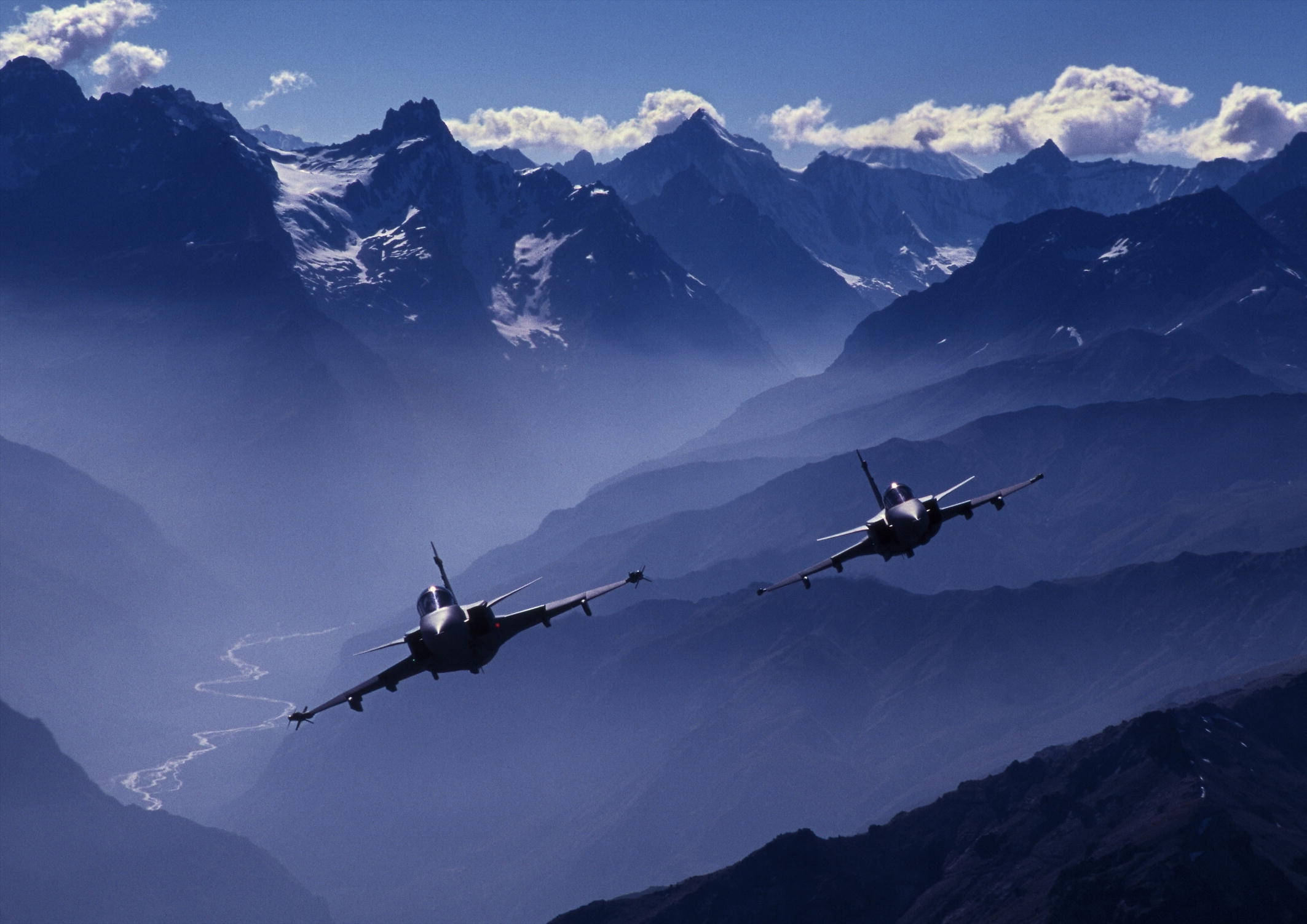 Air Force 桌布 壁紙 — 兩架戰鬥機在晴朗的藍天中翱翔，飛越白雪覆蓋的山峰，下方是霧氣繚繞的山谷。