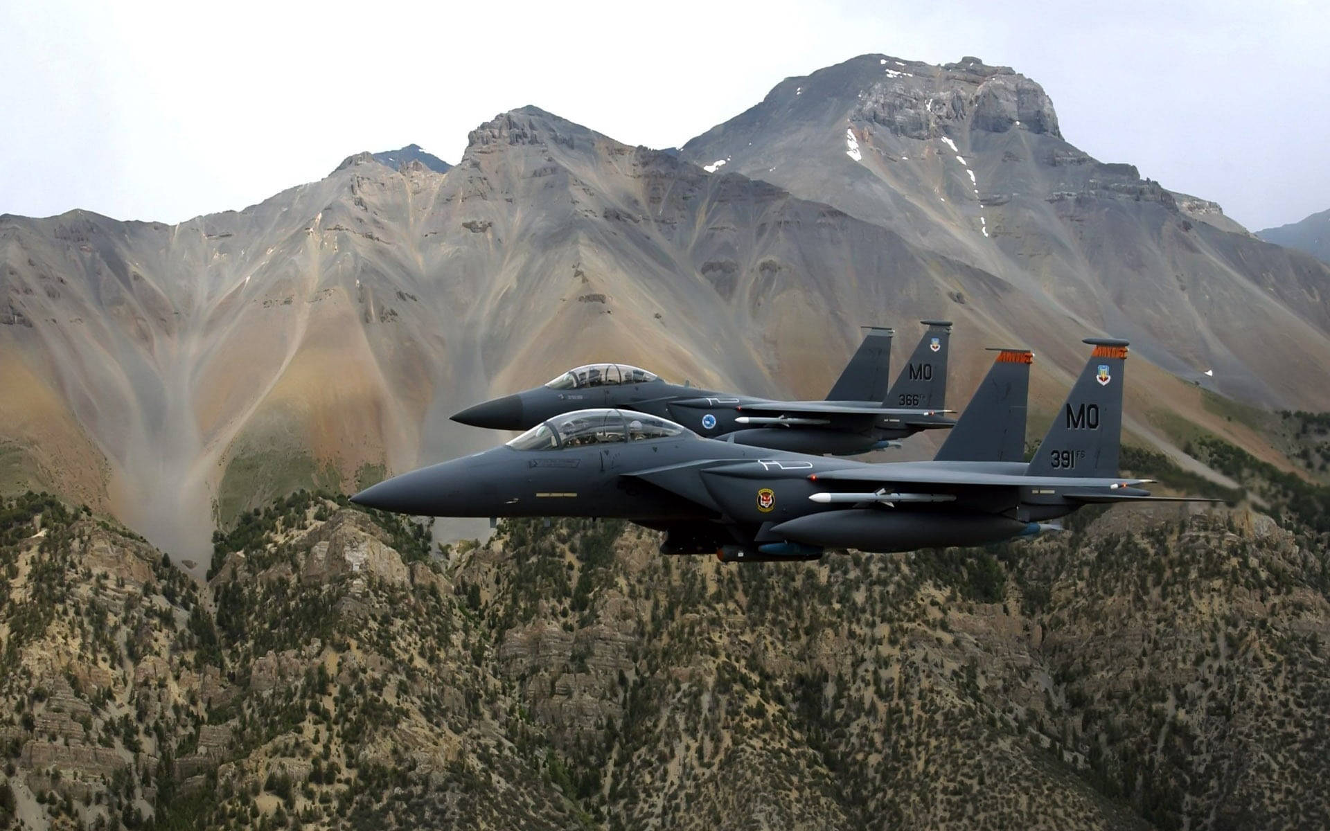軍事動圖 桌布 壁紙 — 兩架戰鬥機在陰天的天空下，於崎嶇的雪山上方編隊飛行。
