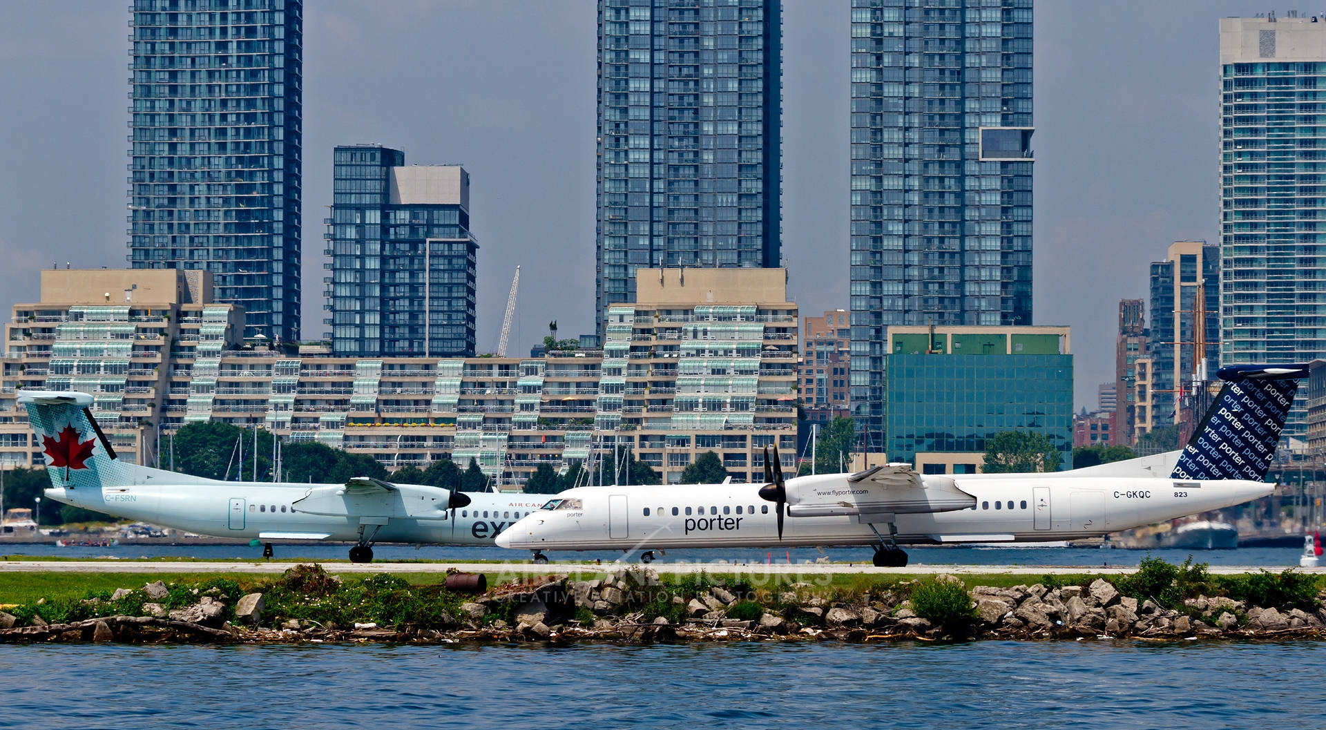 Airport 桌布 壁紙 — 兩架波特航空的渦輪螺旋槳飛機停在跑道旁，旁邊有水，背後有現代玻璃摩天大樓聳立。