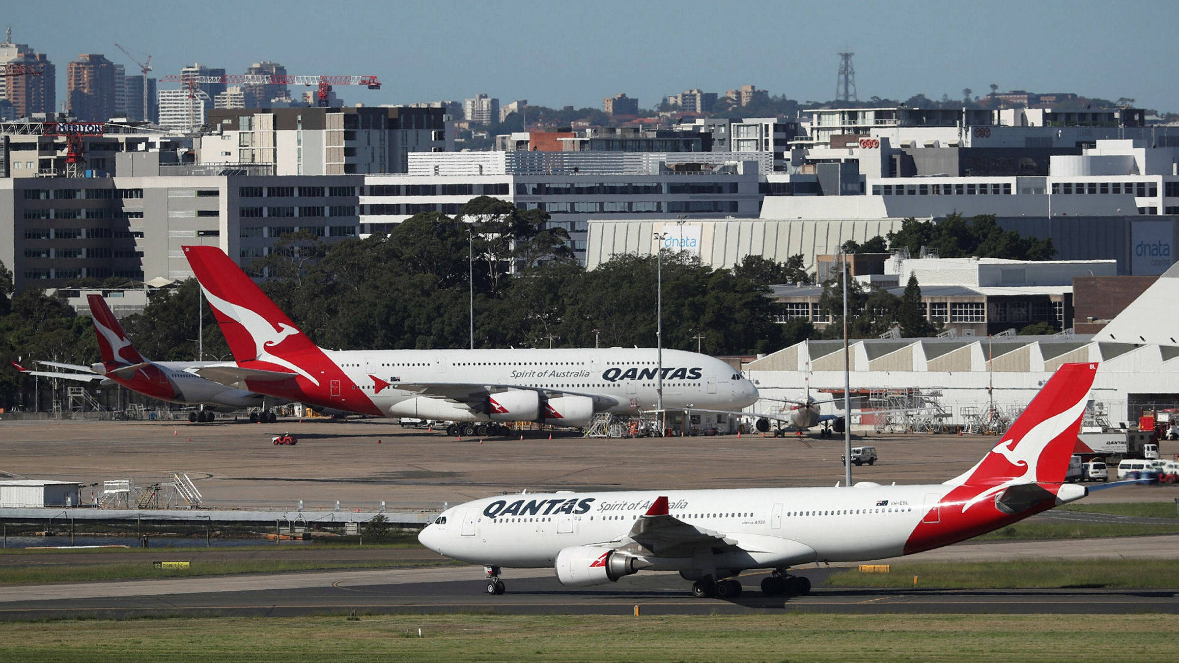 Airport 桌布 壁紙 — 兩架澳洲航空飛機停泊在機場停機坪上，背景是城市天際線，天空清澈湛藍。