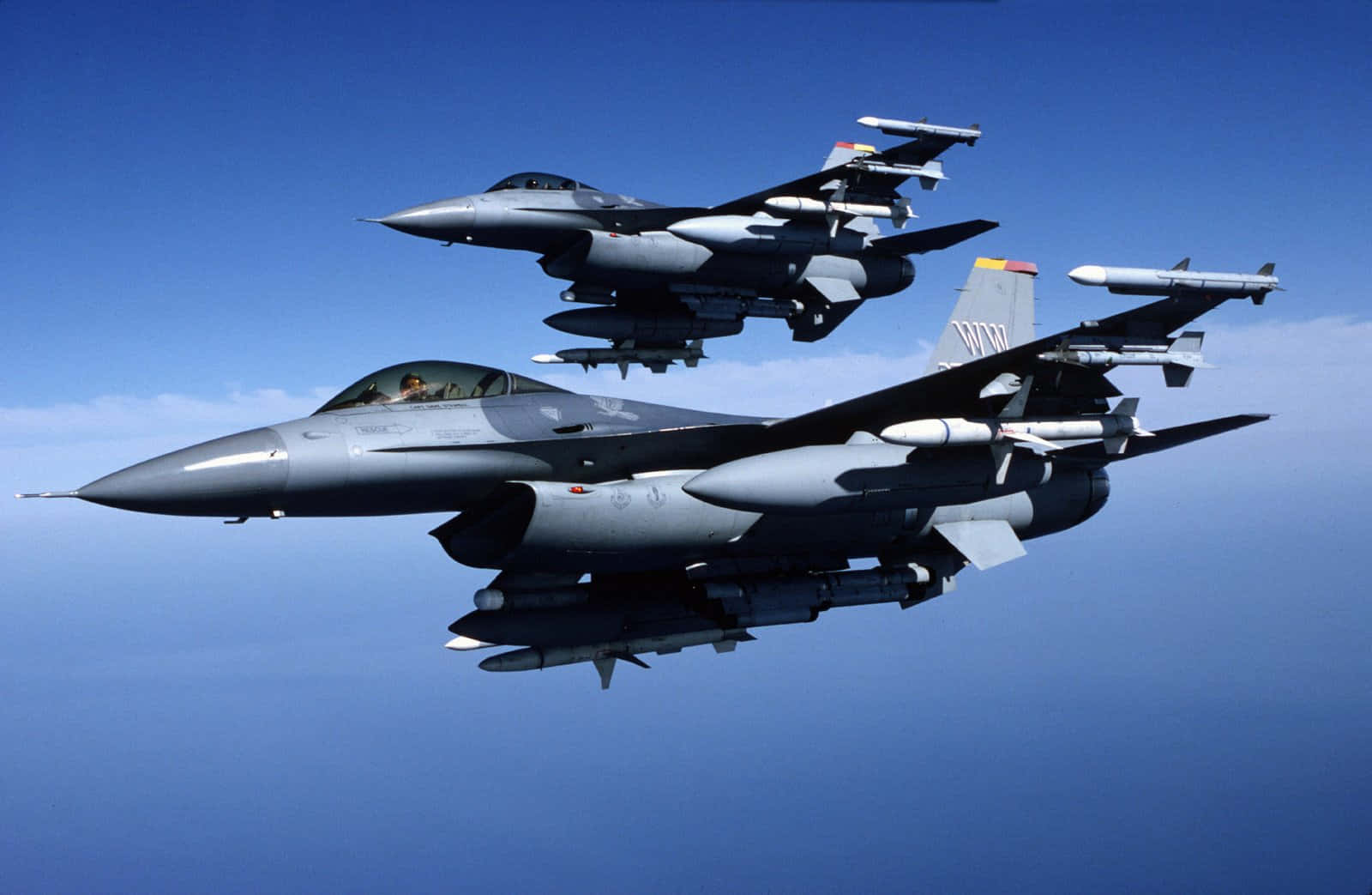 Air Force 桌布 壁紙 — 兩架灰色戰鬥機在晴朗藍天中以編隊翱翔，可見飛彈及駕駛艙內的飛行員。