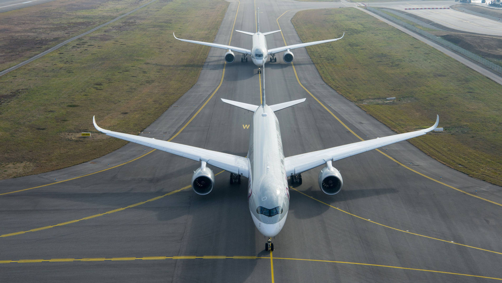 Runway 桌布 壁紙 — 兩架白色客機停在帶有黃色標記的跑道上，跑道兩旁是草地，天空晴朗。