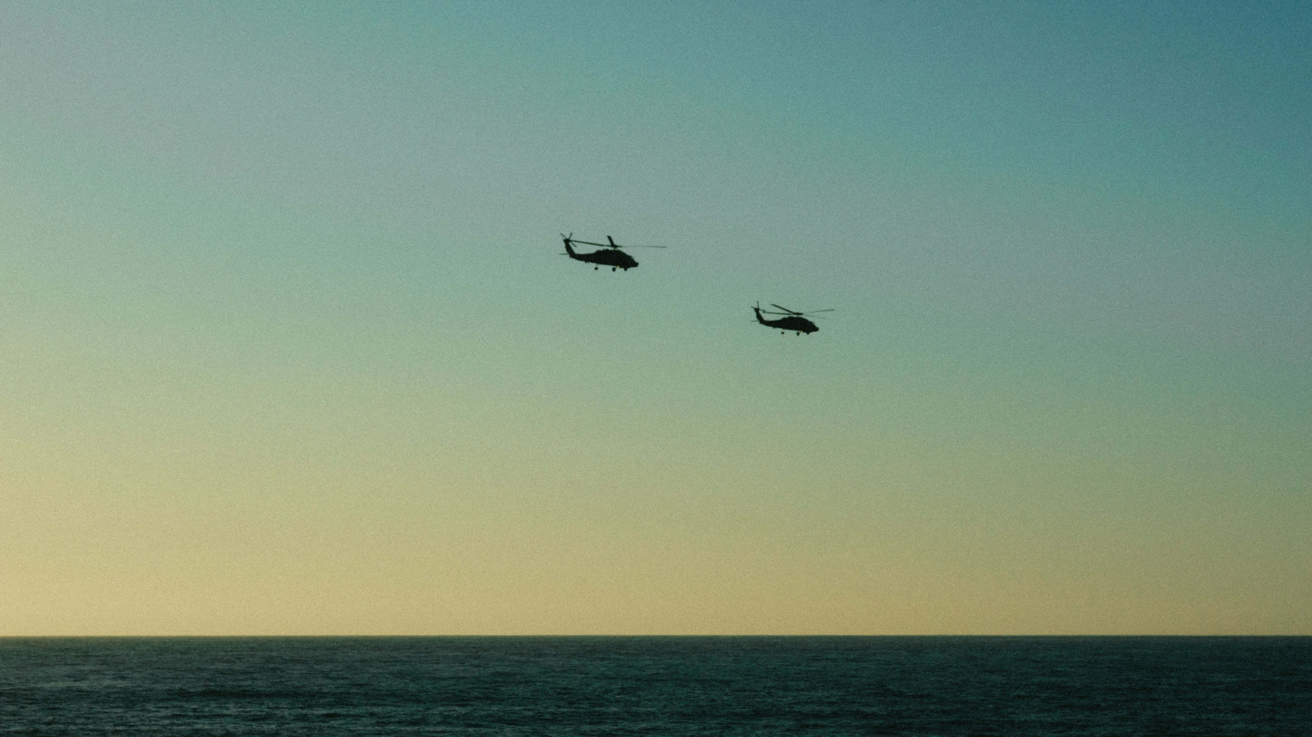 Helicopter 桌布 壁紙 — 兩架直升機在日落時分編隊飛行於平靜的海洋上空，天空呈現漸變色彩。