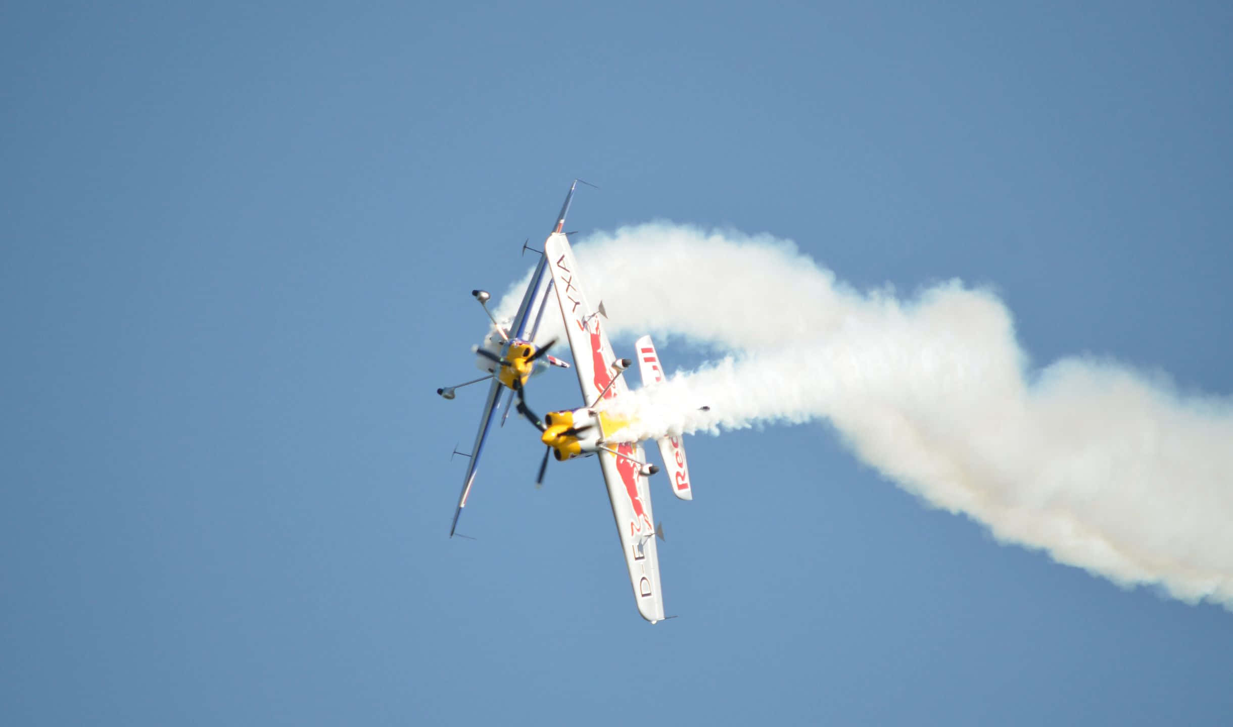 2440x1440 Small Planes 桌布 壁紙 — 兩架紅牛特技飛機在清澈的藍天下進行緊密的空中機動，留下濃厚的白色煙霧痕跡。