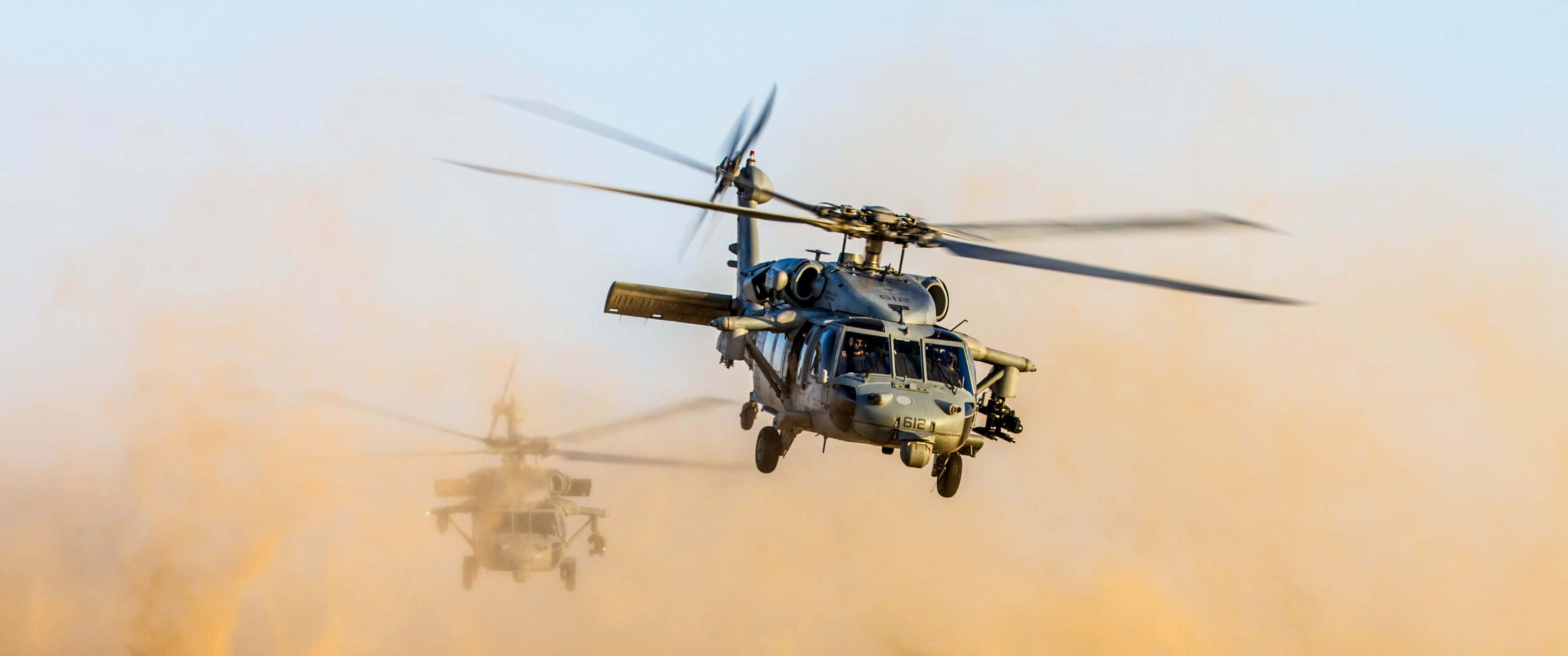 3440x1440p Helicopters 桌布 壁紙 — 兩架軍用直升機低飛穿過塵霧，旋翼槳葉因運動而模糊。