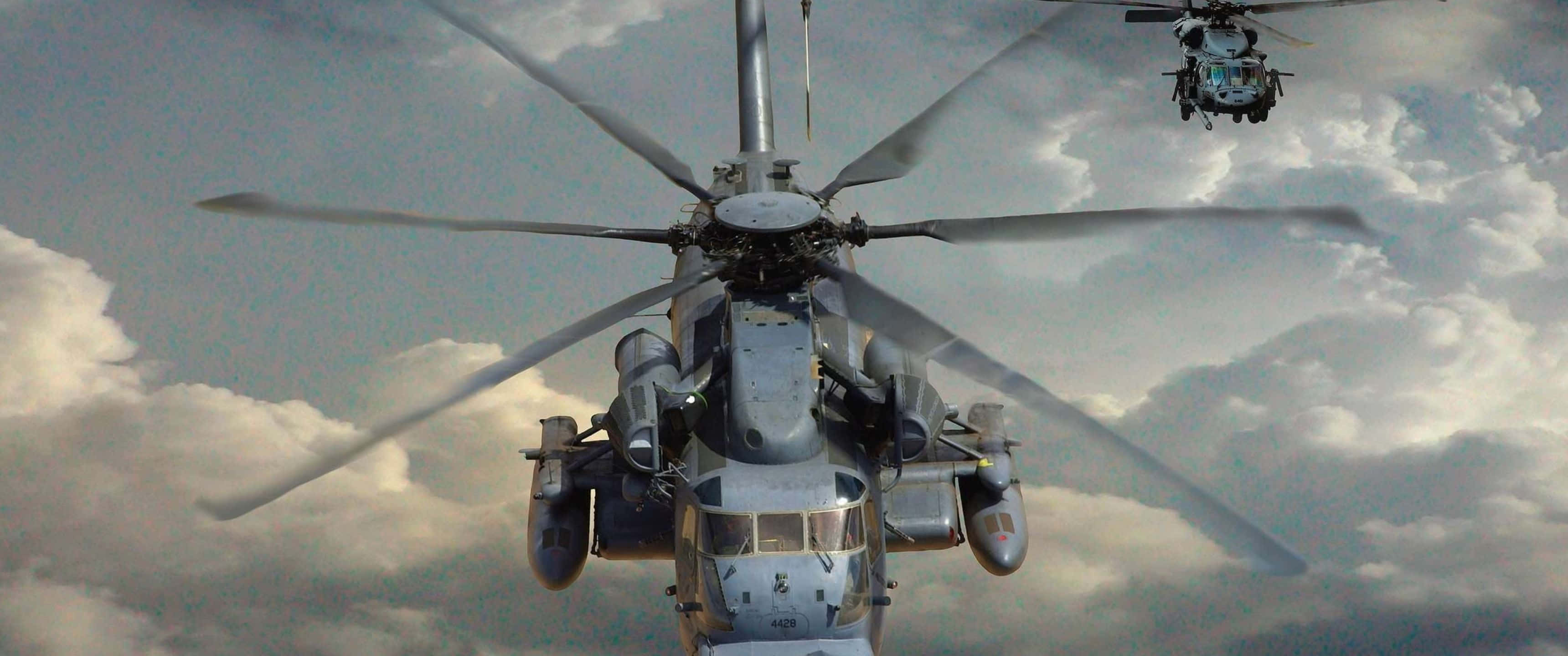 3440x1440p Helicopters 桌布 壁紙 — 兩架軍用直升機在多雲的天空中編隊飛行，旋翼槳葉因運動而模糊。