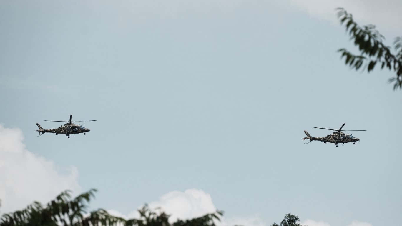 1366x768 Helicopters 桌布 壁紙 — 兩架軍用直升機在淡藍色的天空下編隊飛行，下方可見散落的雲朵和樹梢。