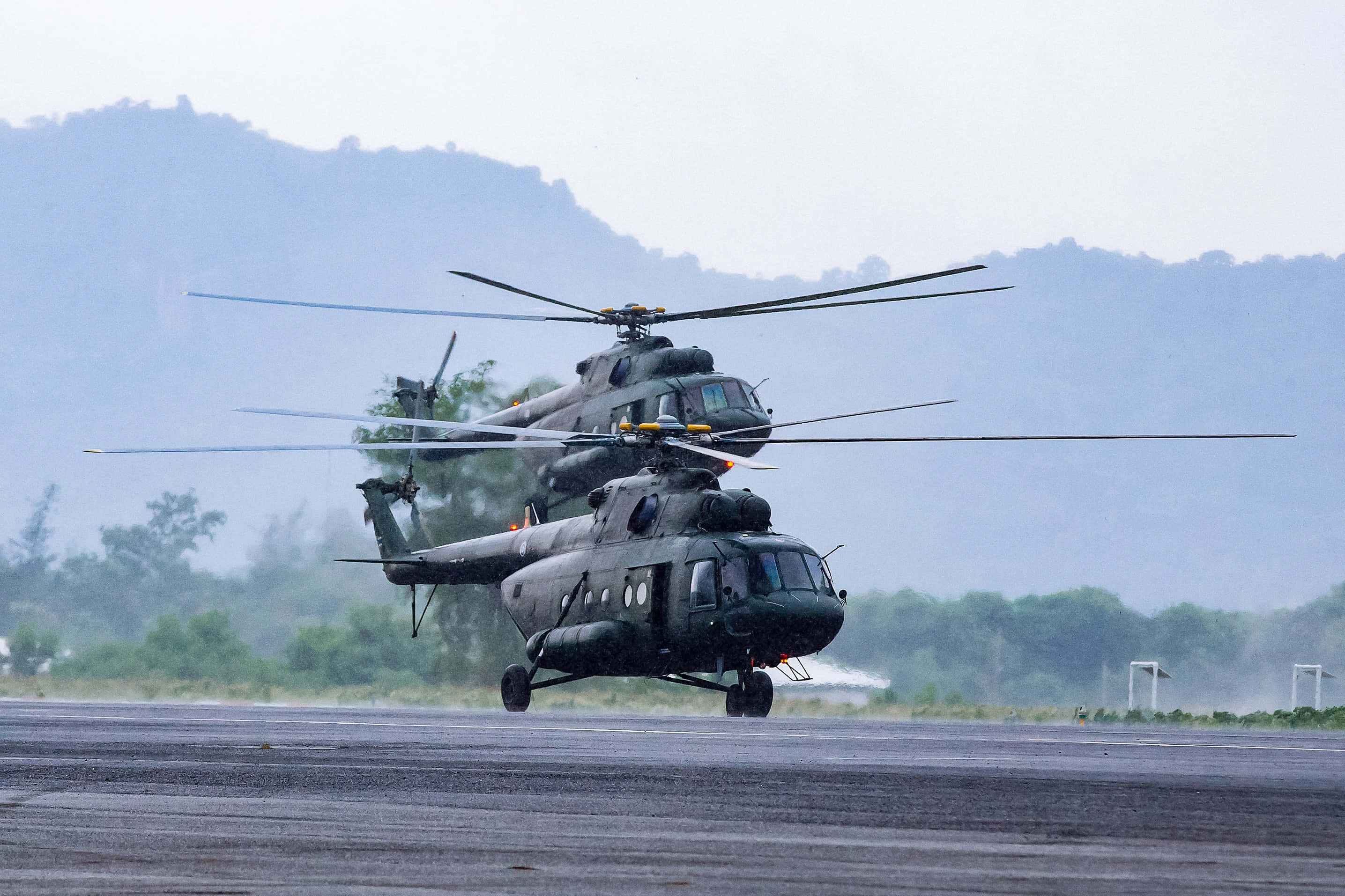Helicopter 桌布 壁紙 — 兩架軍用直升機在潮濕的跑道上低空盤旋，背景是霧氣繚繞的山巒。