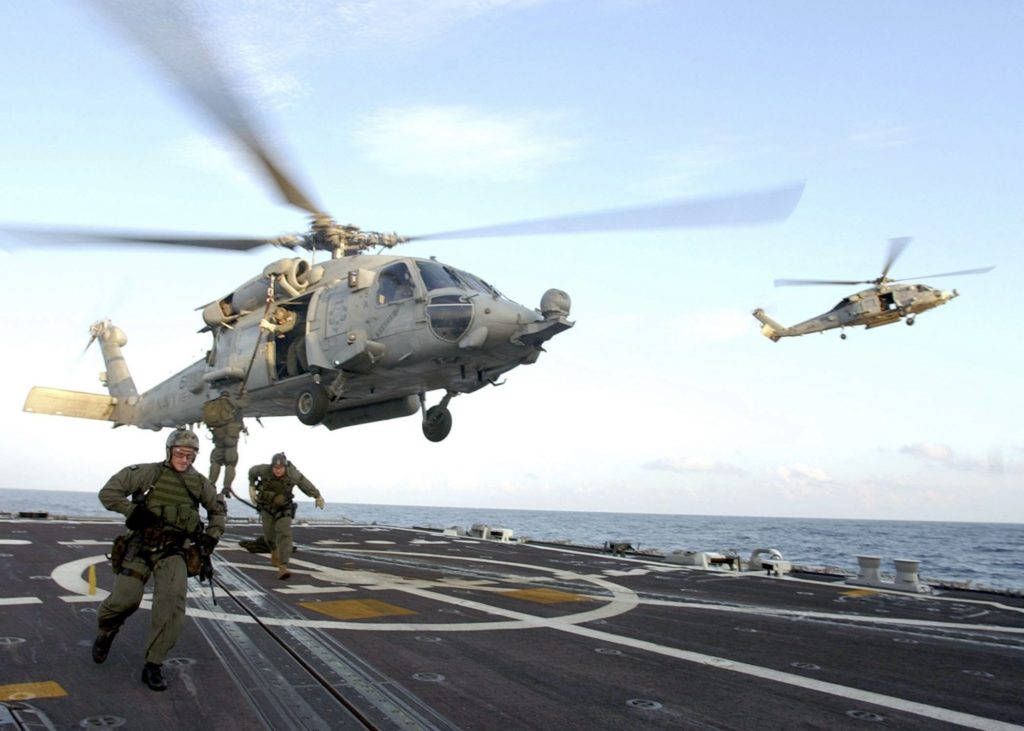 Helicopter 桌布 壁紙 — 兩架軍用直升機在航空母艦甲板上空盤旋，水兵們在晴朗的藍天下向船邊衝刺。