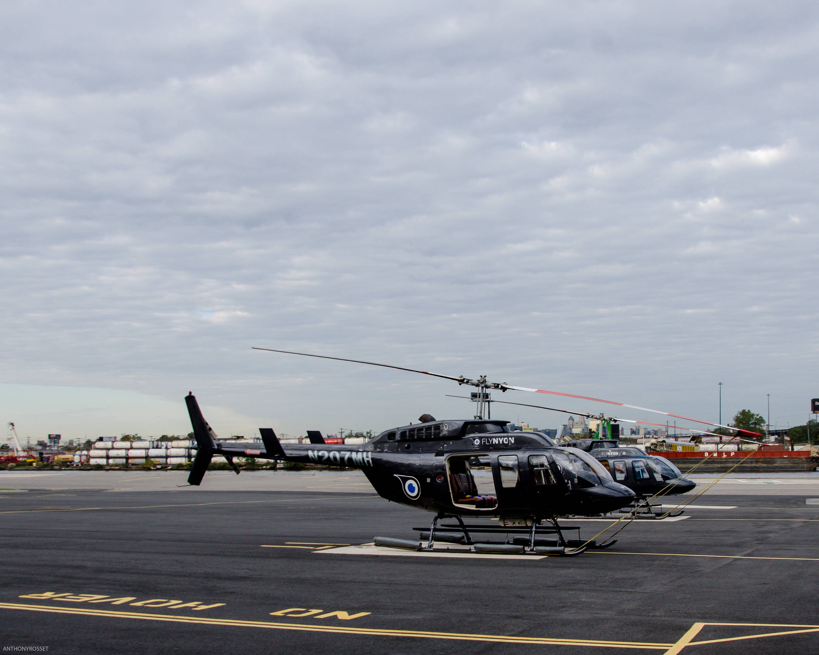 Helicopter 桌布 壁紙 — 兩架黑色直升機停泊在停機坪上，天空多雲，背景有工業建築。