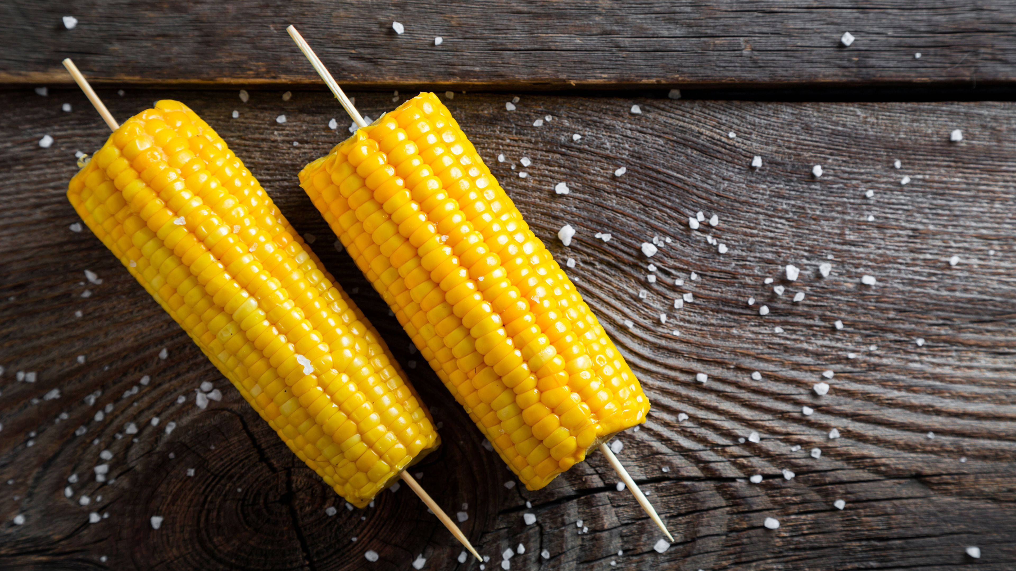 Corn 桌布 壁紙 — 兩根鹽味玉米串放在風化的木質表面上，散落著粗鹽。