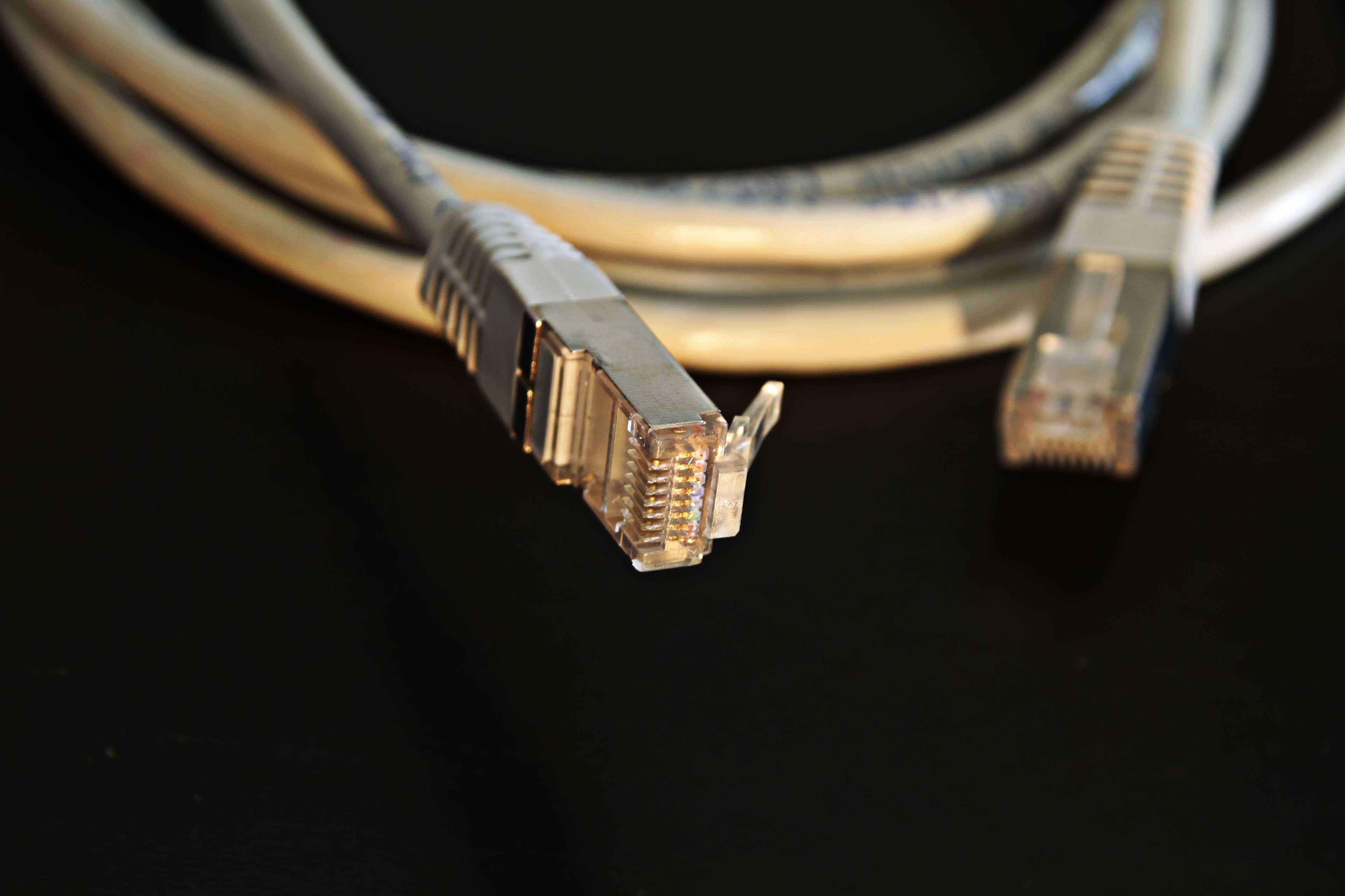 Ethernet 桌布 壁紙 — 兩條乙太網路電纜盤繞在黑色表面上，對連接器進行銳利對焦的特寫。