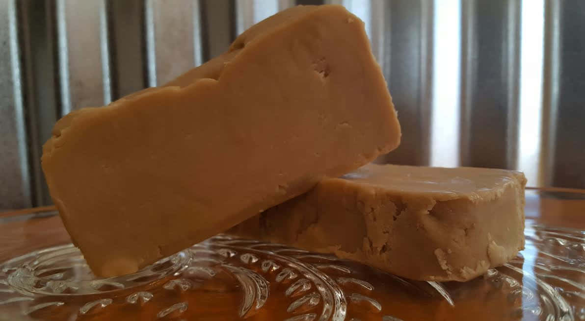 Penuche Fudge 桌布 壁紙 — 兩條光滑的焦糖色軟糖棒放在一個華麗的玻璃盤上，背景是波紋金屬。