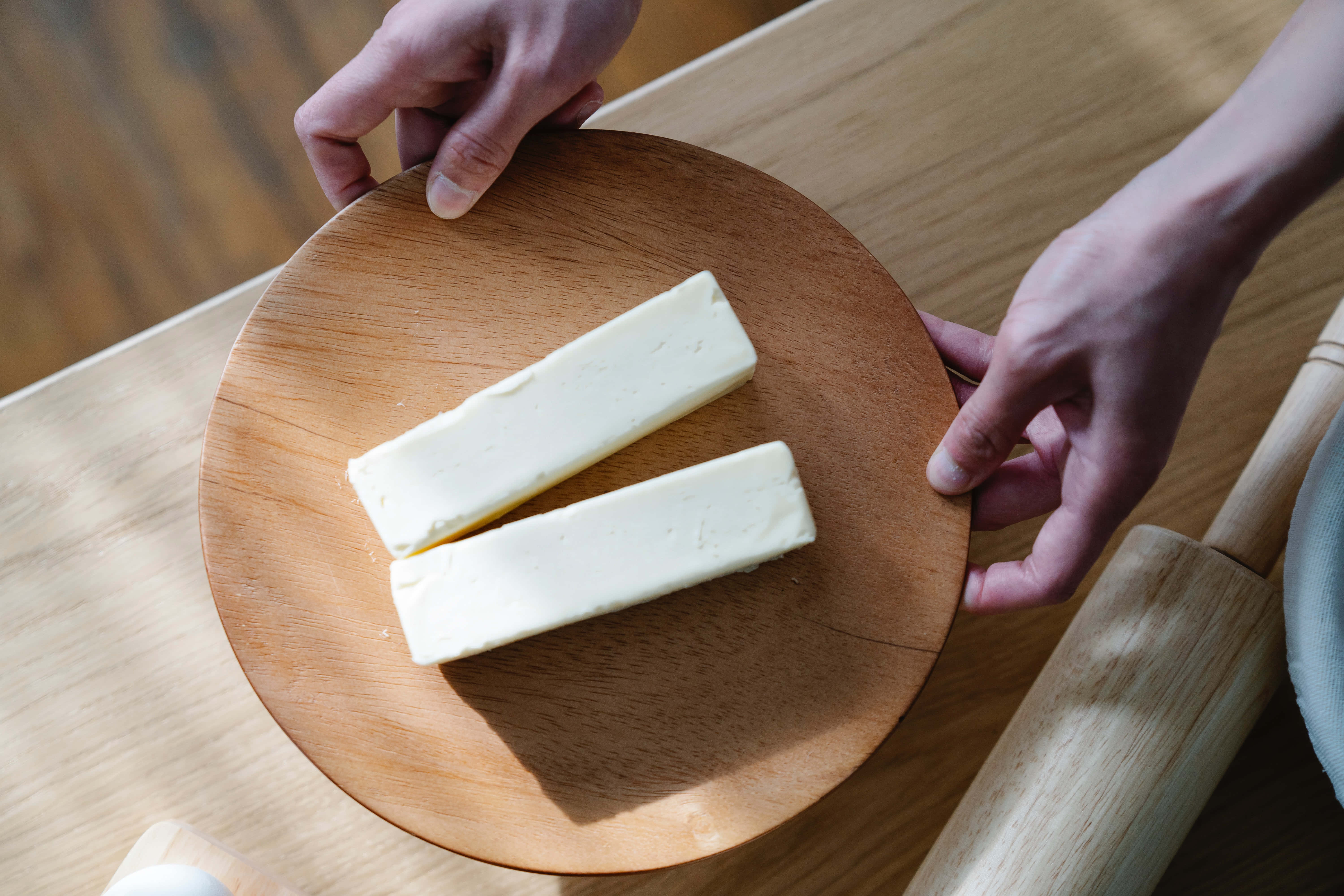 Cheese 桌布 壁紙 — 兩條奶油放在一個由手拿著的木板上，在一個溫暖的廚房環境中。