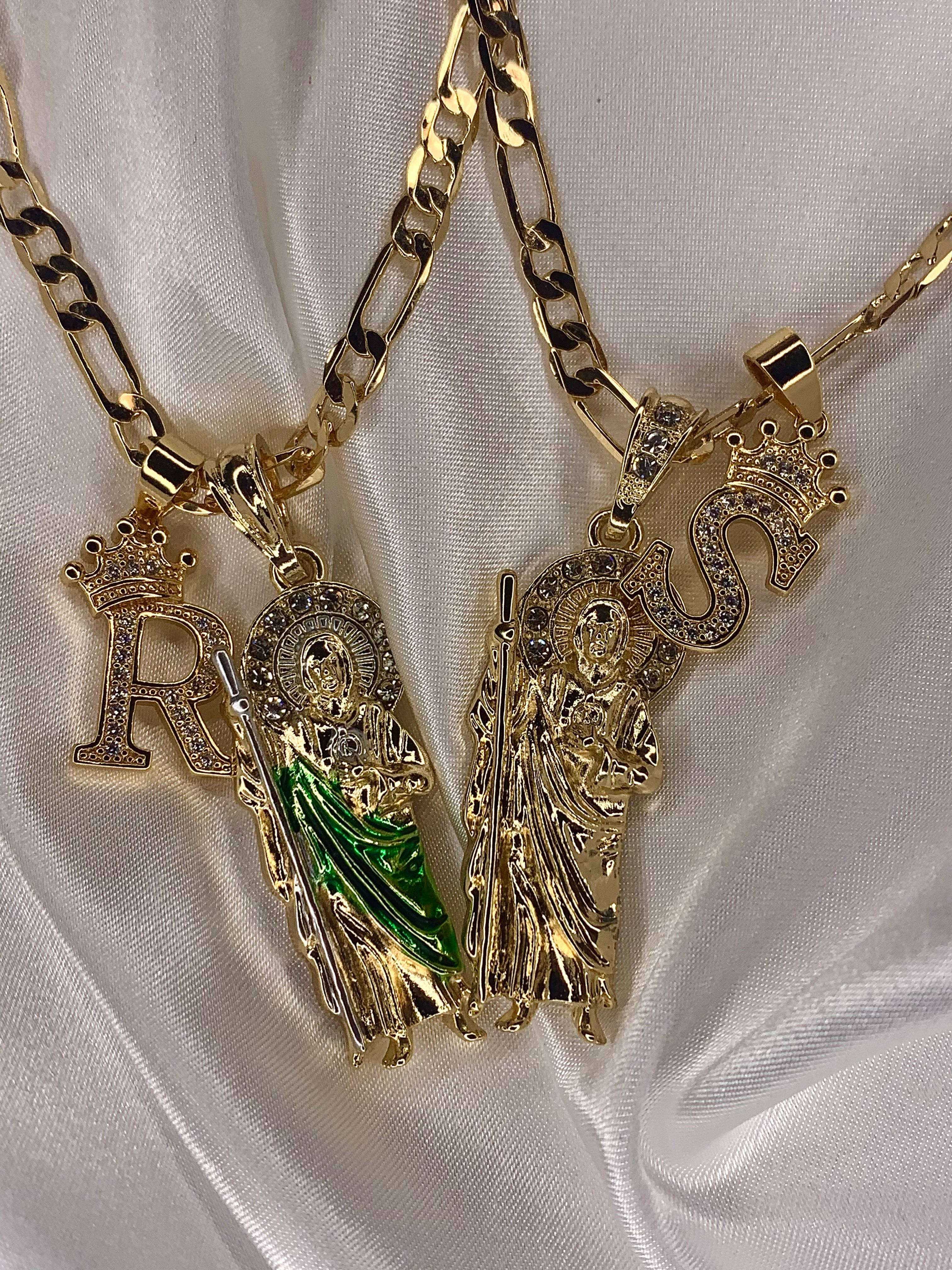 religion 桌布 壁紙 — 兩條帶有宗教人物吊墜和寶石字母飾物的金鏈放在白色緞布上。