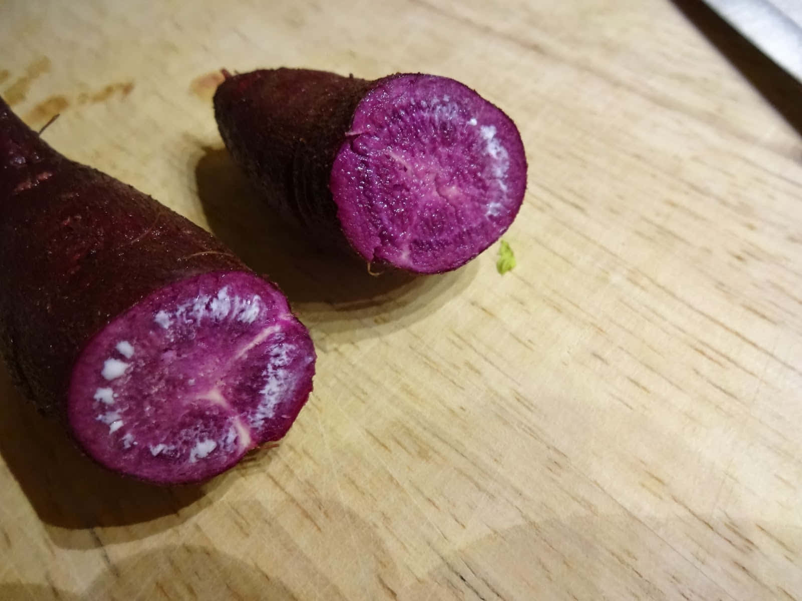 Purple Potato 桌布 壁紙 — 兩條帶有白色斑點的紫色蘿蔔切片放在淺色木砧板上。