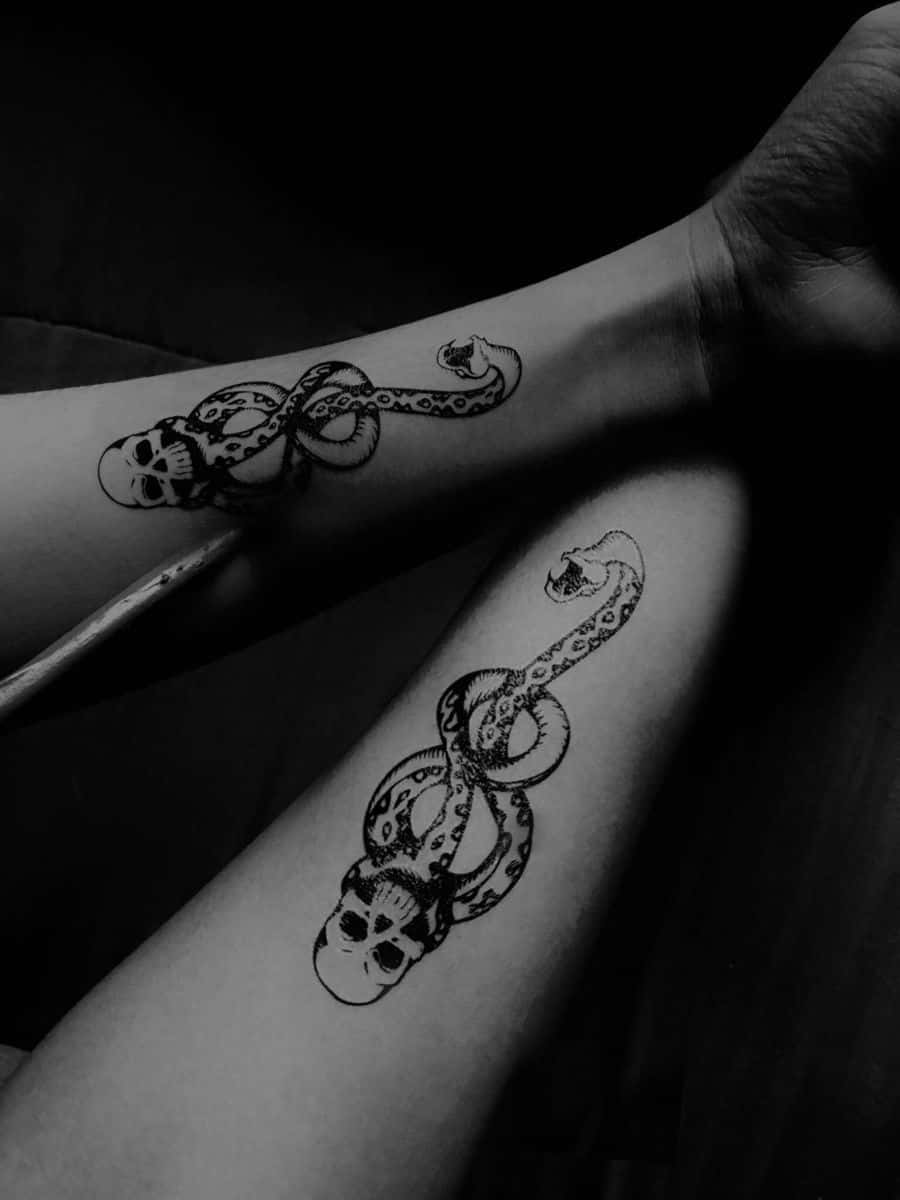 Death Eaters 桌布 壁紙 — 兩條手臂展示蛇纏繞頭骨的複雜黑白刺青，背景為深色。