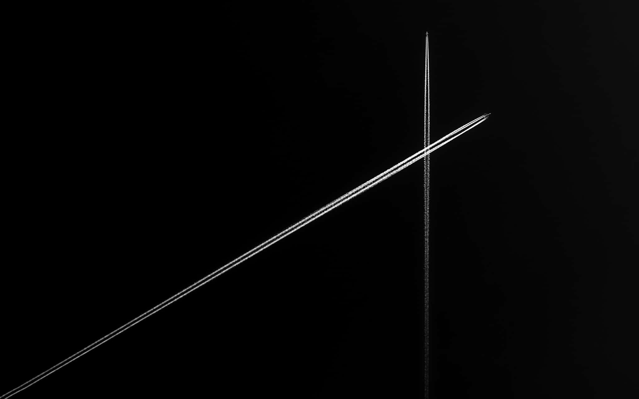 Minimalist Monochrome 桌布 壁紙 — 兩條相交的飛機雲在深黑色天空中形成一個鮮明的十字架，高對比度黑白影像。
