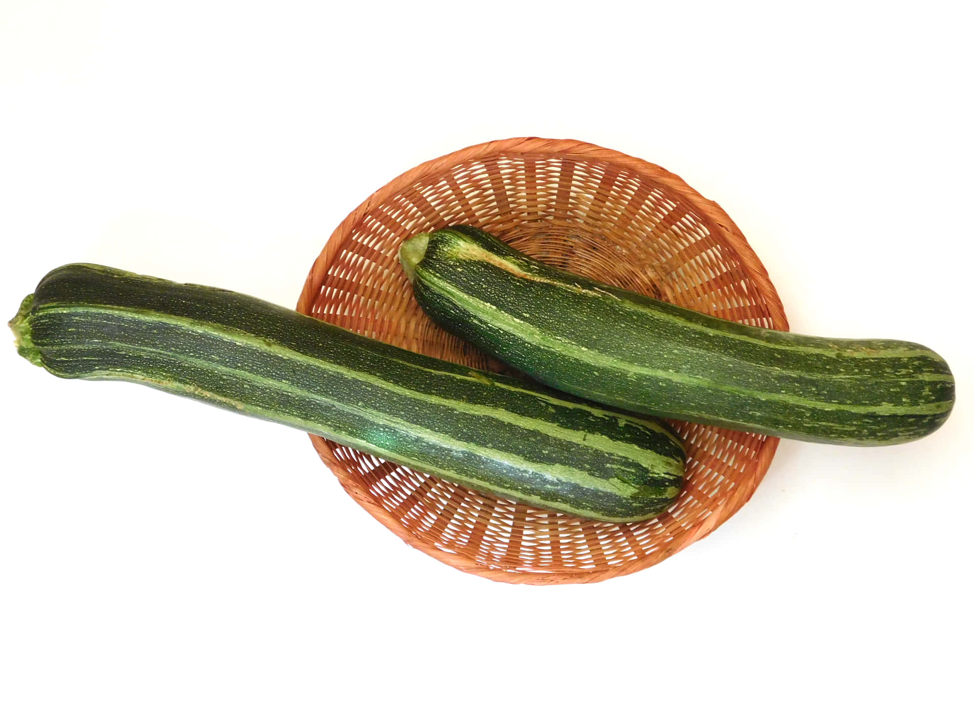 Zuchinis 壁紙 — 兩條綠色條紋櫛瓜放在一個圓形編織籃子上，背景為純白色。