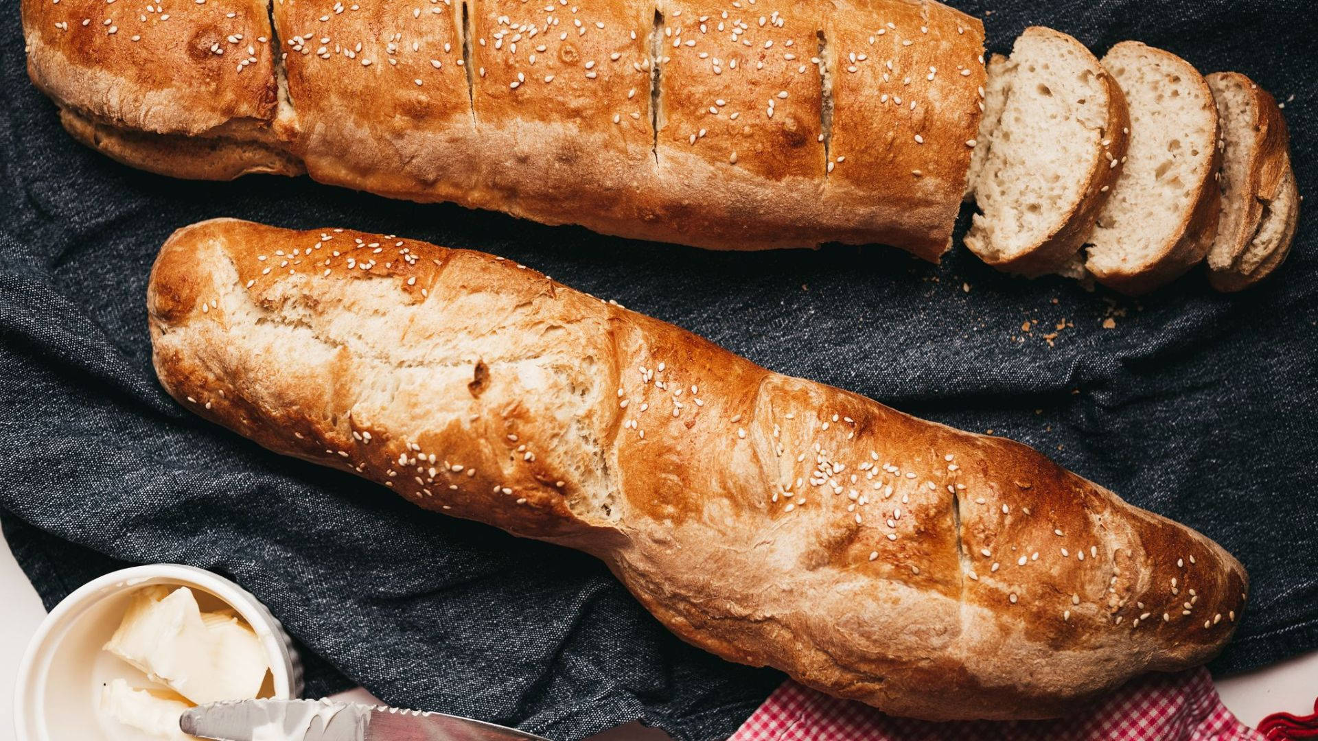 Bread 桌布 壁紙 — 兩條金黃芝麻法棍麵包切片，配上奶油，放在深色布上。
