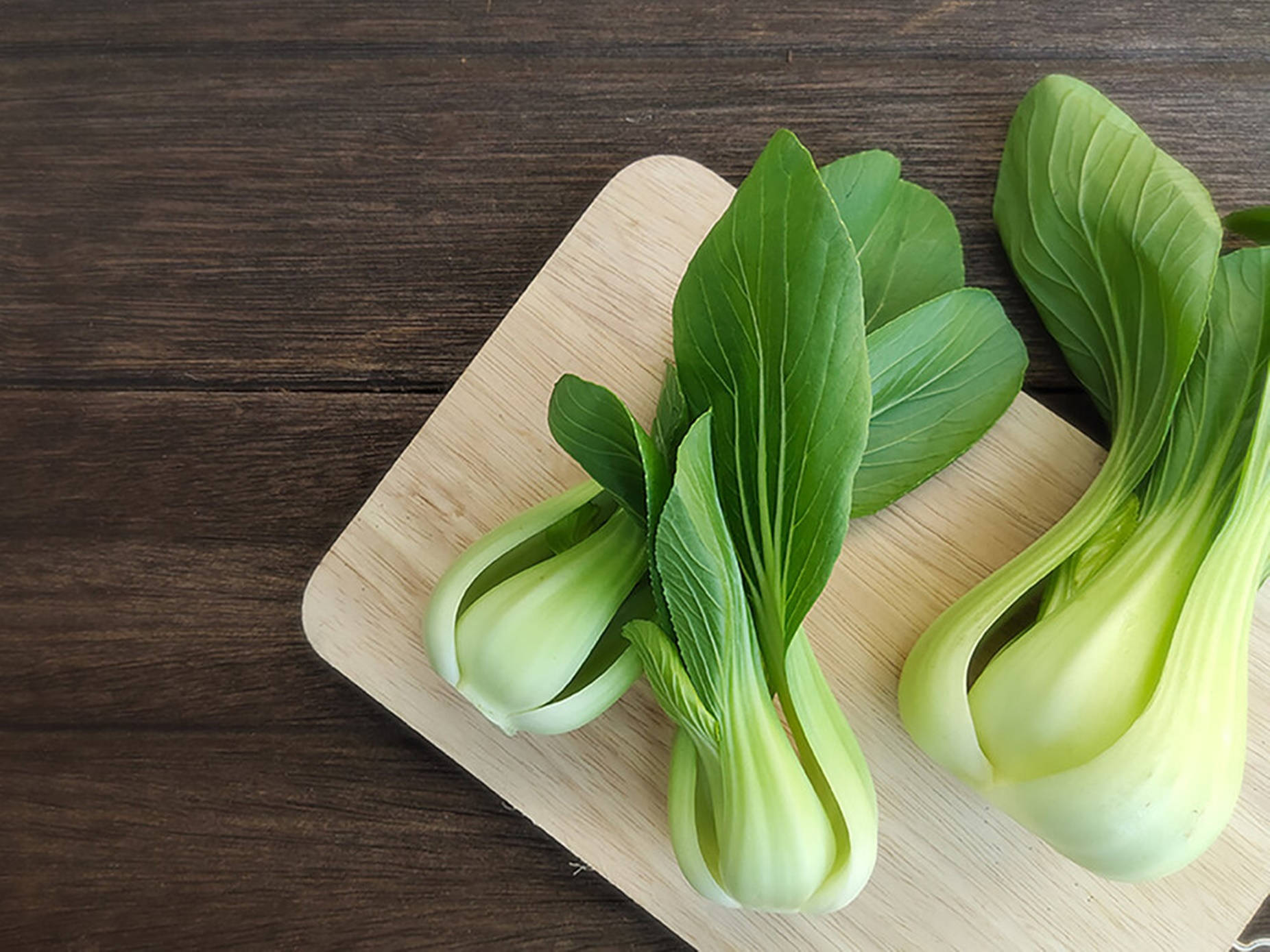 Vegetables 桌布 壁紙 — 兩棵新鮮小白菜放在淺色木砧板上，砧板置於深色鄉村風木桌上。