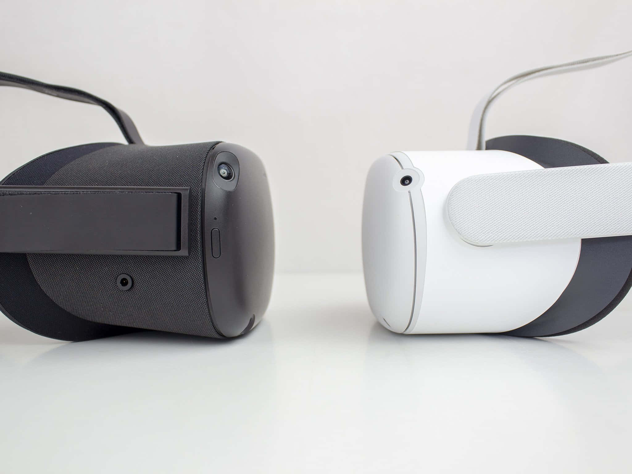 Oculus Quest 2 桌布 壁紙 — 兩款時尚的VR頭戴式裝置，黑色和白色，並排放在簡約的白色表面上。