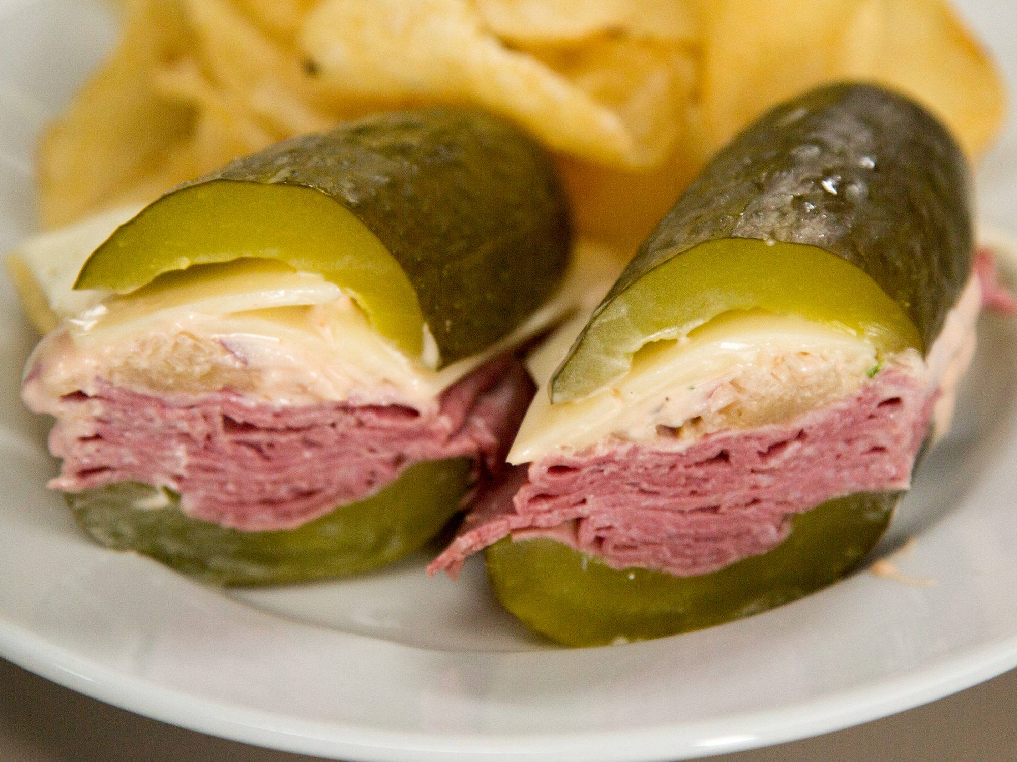 Pickle 桌布 壁紙 — 兩片酸黃瓜夾著熟食肉、起司和醬汁，放在白色盤子上，後面有薯片。