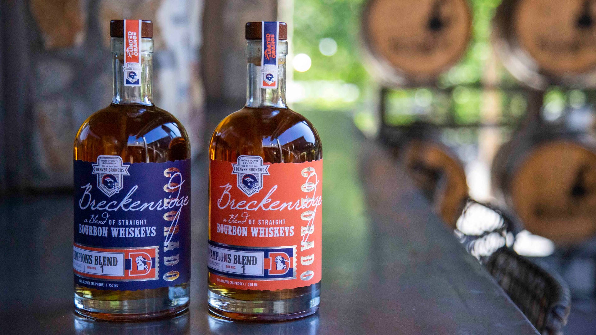drinks 桌布 壁紙 — 兩瓶 Breckenridge 波本威士忌，帶有藍色和橙色標籤，放在一張深色桌子上，背景中木桶模糊。