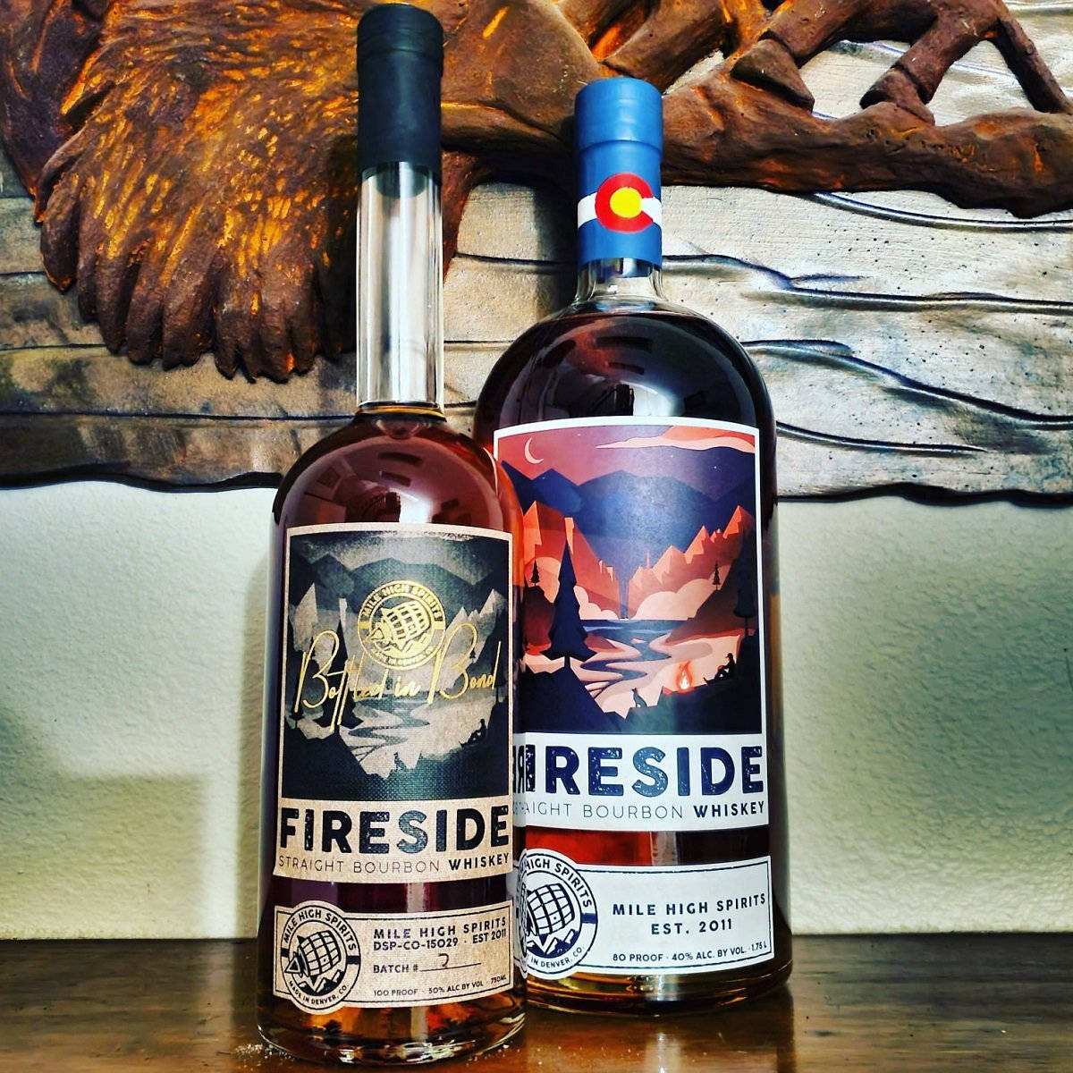 alcohol 桌布 壁紙 — 兩瓶 Mile High Spirits 波本威士忌放在木質表面上，背景是質樸的鷹雕塑。