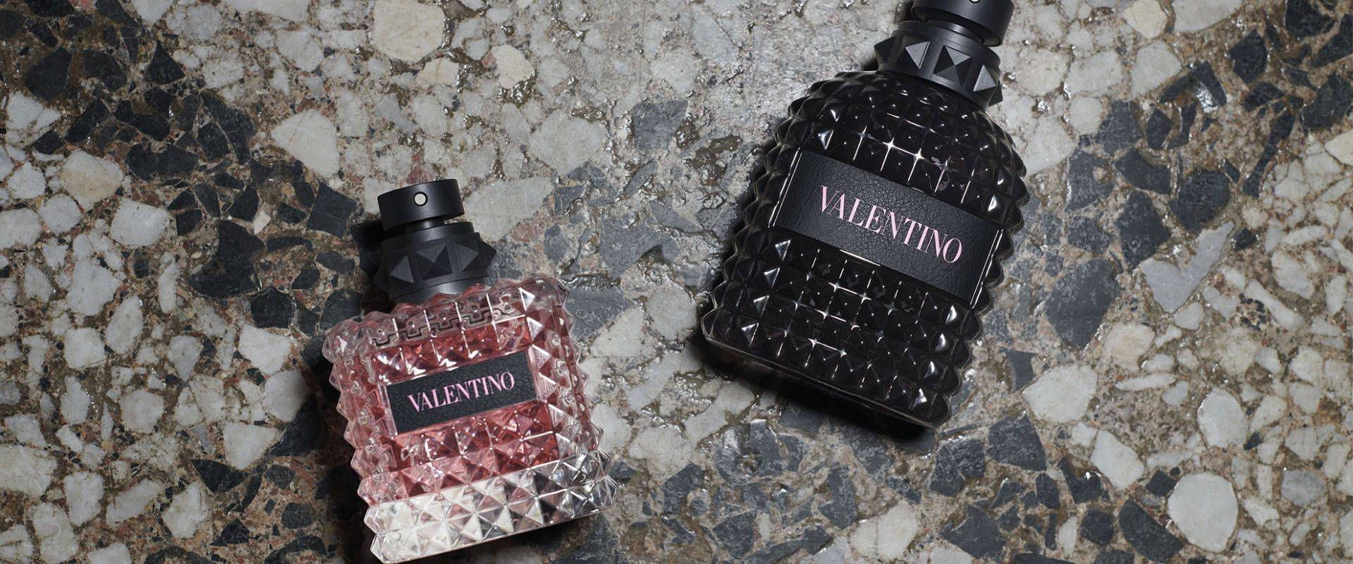 寬螢幕動態圖片 桌布 壁紙 — 兩瓶 Valentino 香水，一瓶透明切割粉紅色，一瓶黑色鉚釘裝飾，放在斑點石面上。